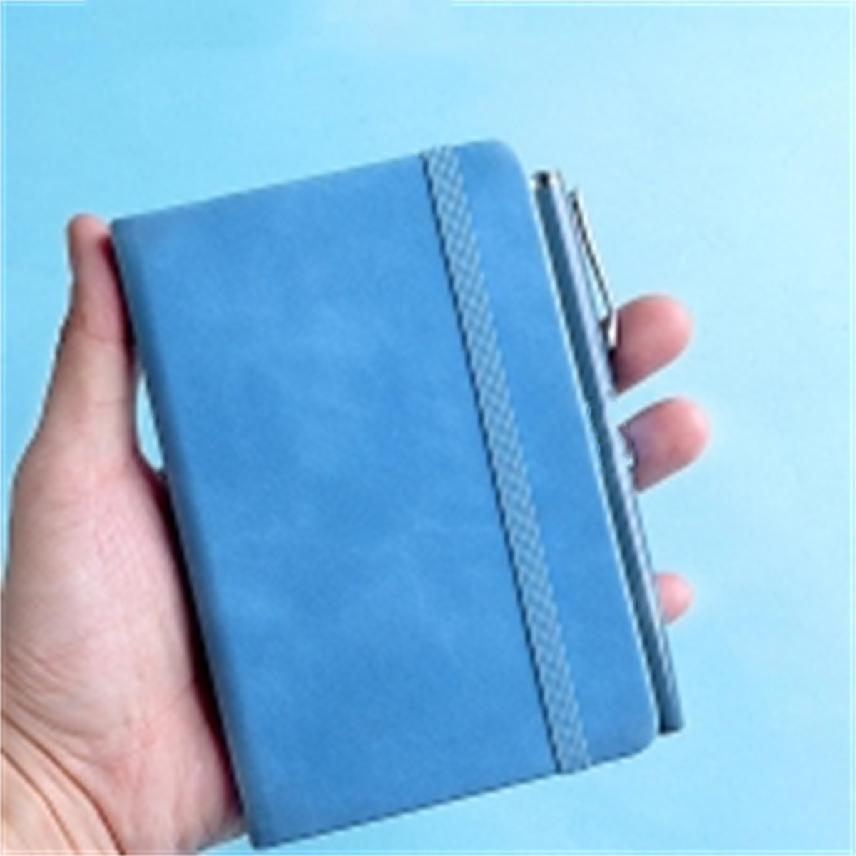 Ein blaues Notizbuch mit Gummiband und Stift, gehalten in einer Hand. Der Hintergrund ist blau.