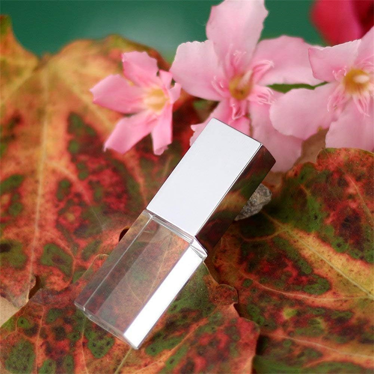 Ein kleiner silberner Parfümflakon auf Herbstblättern und rosa Blüten.