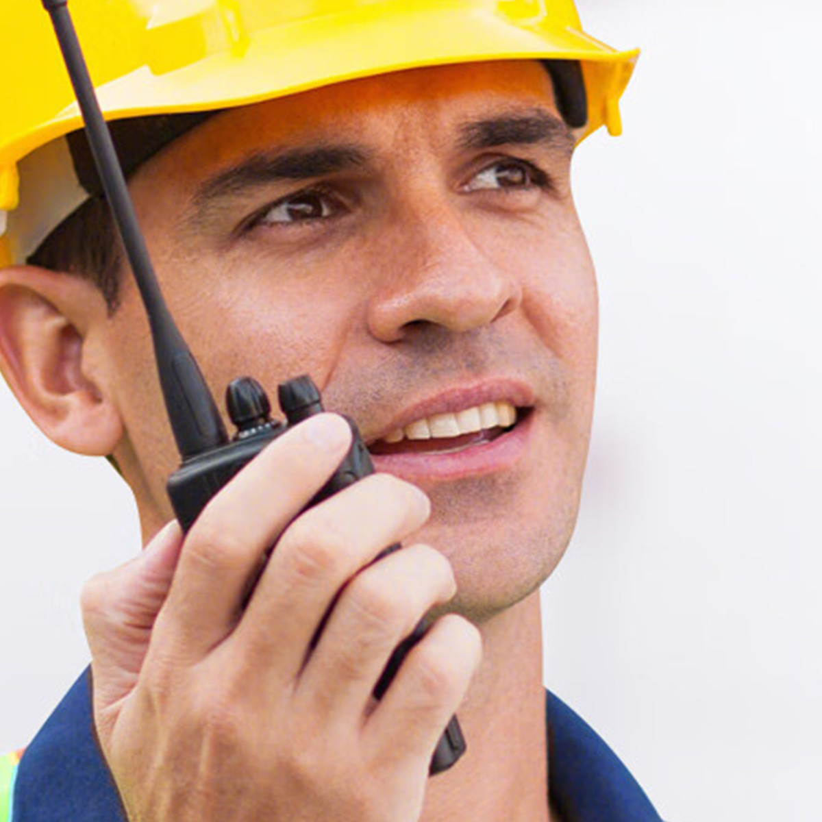Mann mit gelbem Helm hält ein Walkie-Talkie, Blick nach rechts.