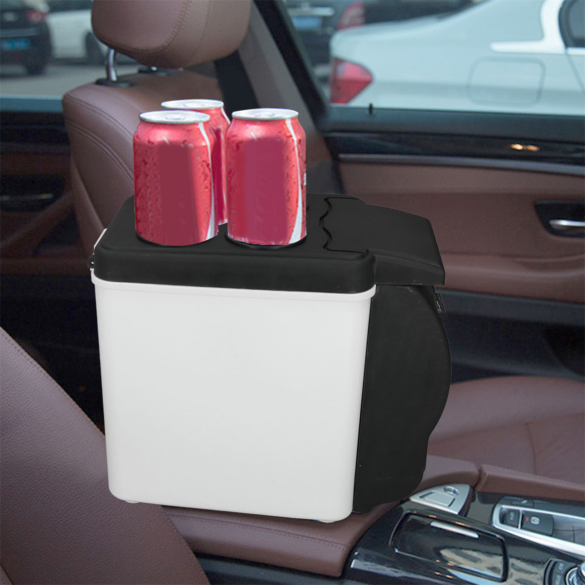 Eine weiße Kühlbox in einem Auto mit drei roten Dosen oben drauf. Innenraum des Autos ist im Hintergrund sichtbar.
