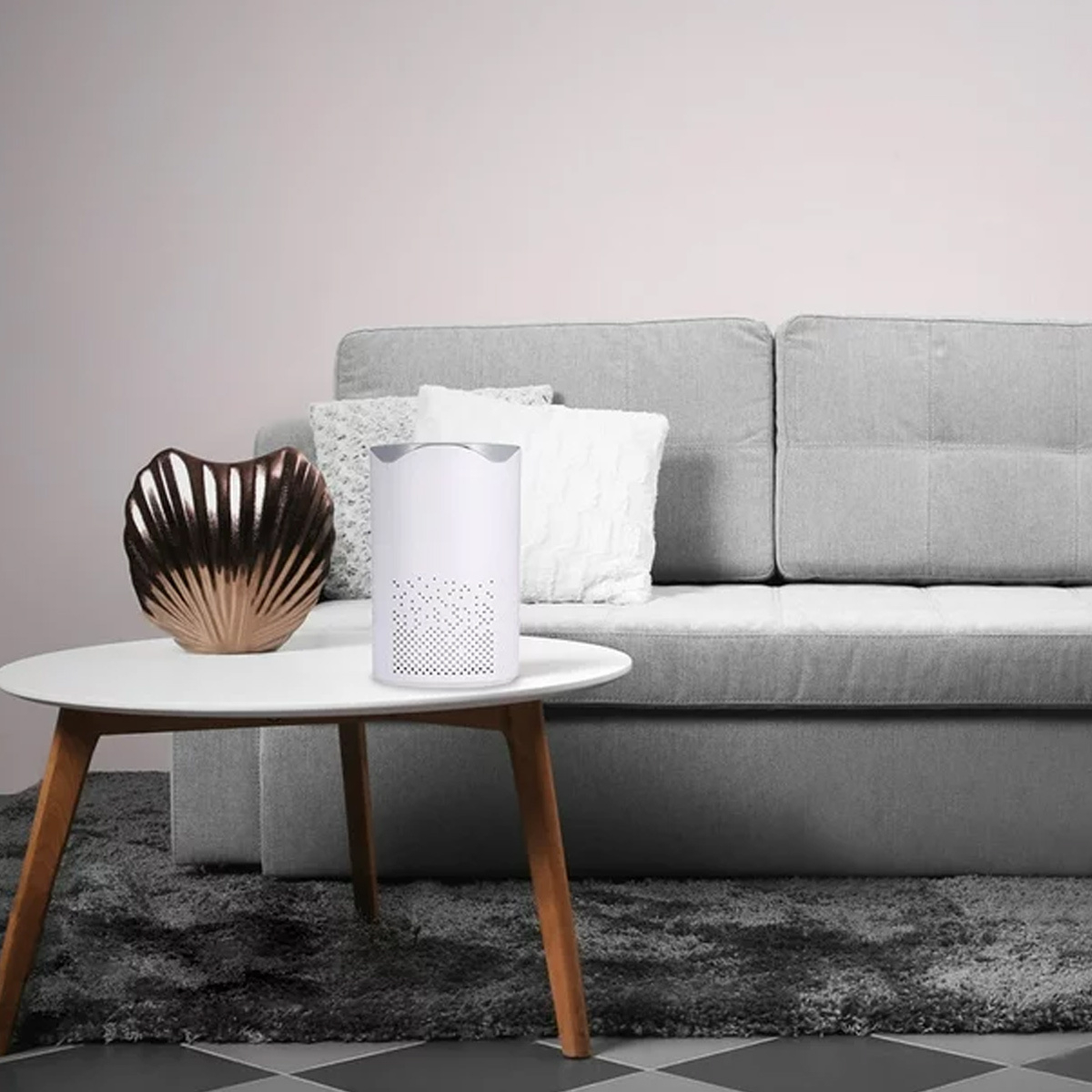 Weißer Luftreiniger und dekorative Muschel auf einem Tisch neben einem grauen Sofa und Teppich.
