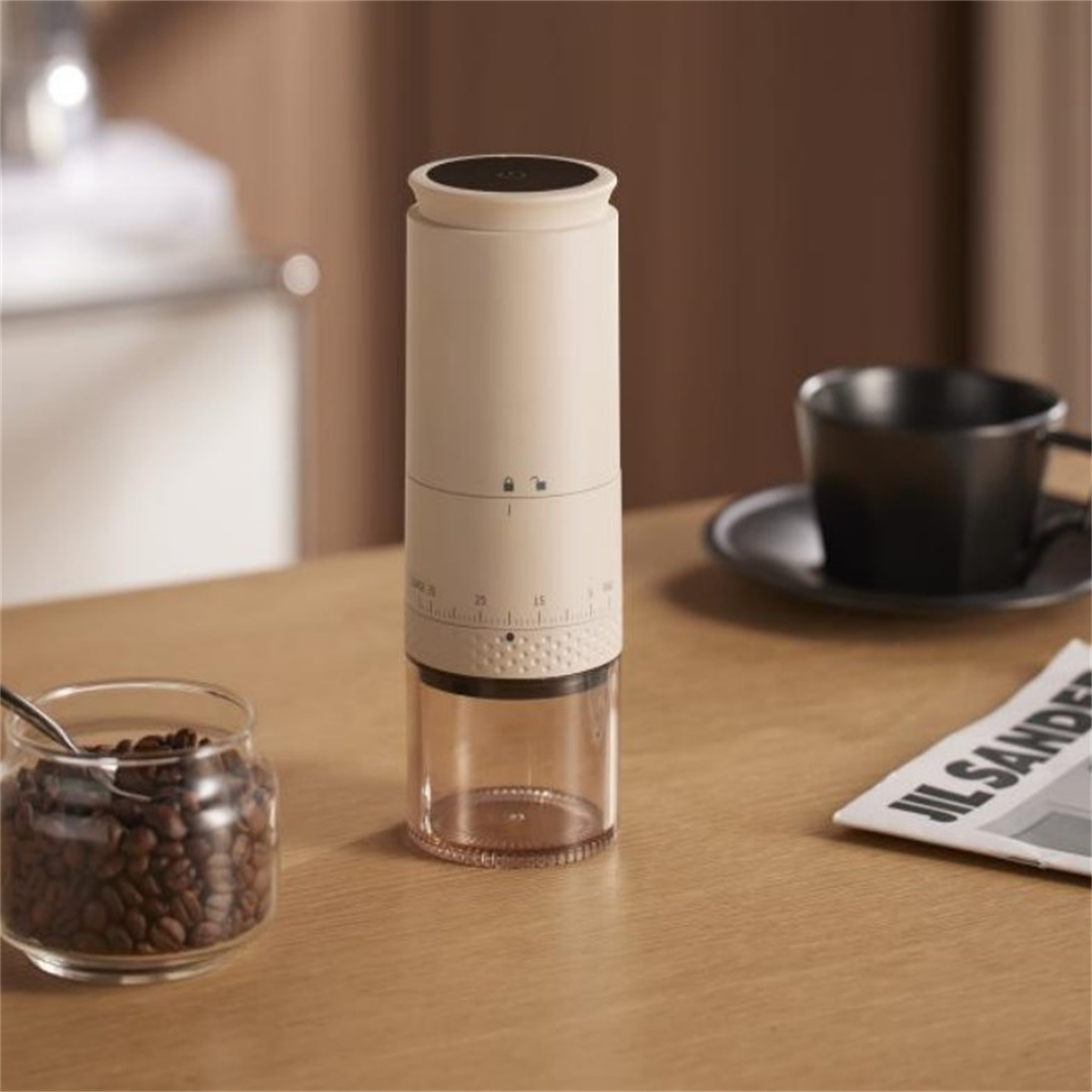 Elektrische Kaffeemühle mit Bohnen im Glas, einer Tasse und Zeitung auf einem Tisch.