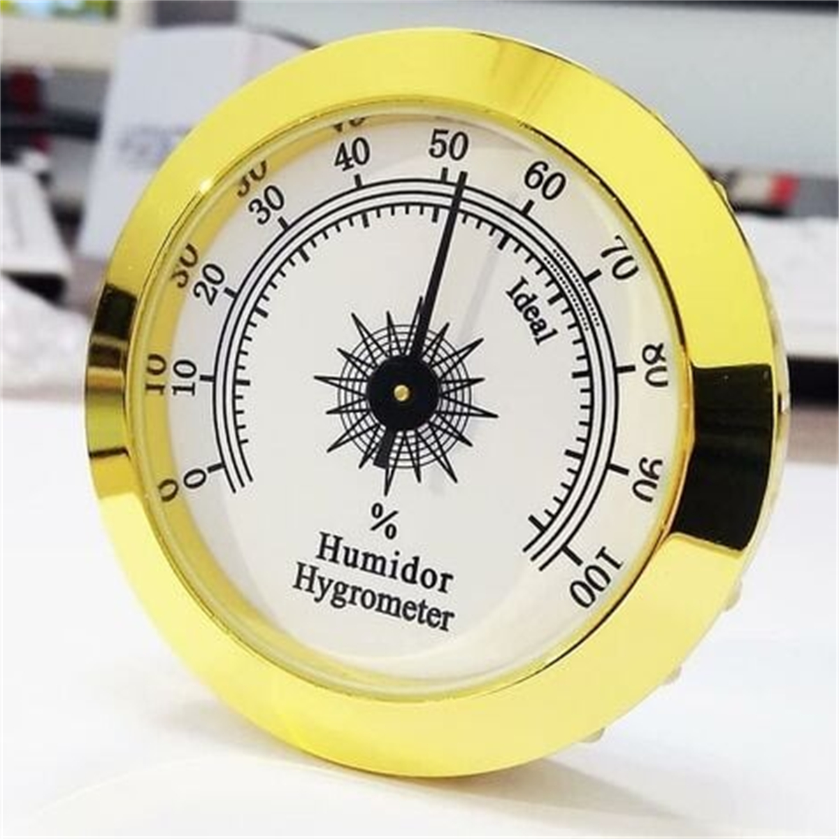 Kreisförmiges Hygrometer mit Goldrand, schwarzer Nadel und weißem Zifferblatt.