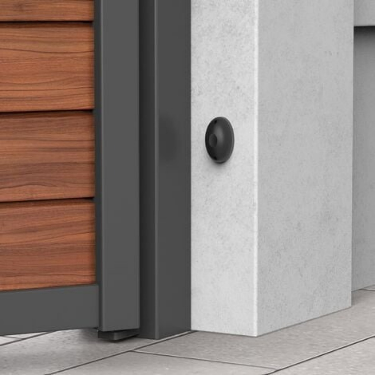 Ein kleiner schwarzer Sensor an einer Betonmauer neben einer Holztür mit Metallrahmen.