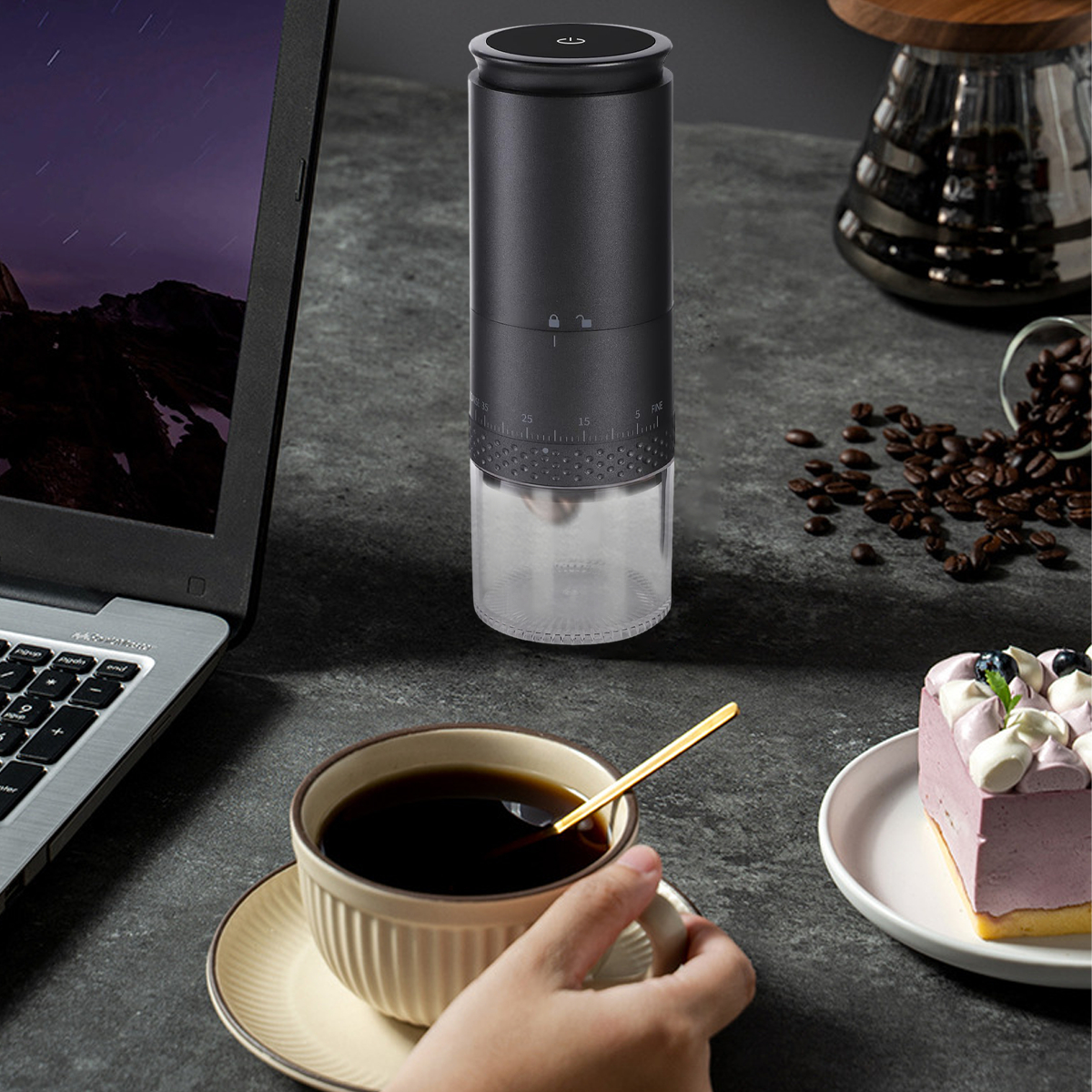 Schwarze Kaffeemühle mit Kaffee und einer Tasse. Ein Laptop steht ebenfalls auf dem Tisch.