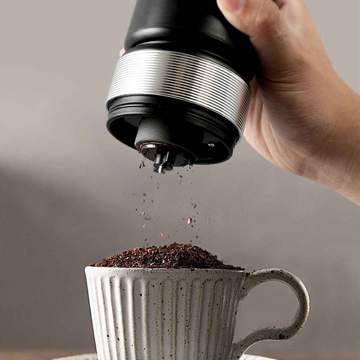 Eine Person gießt gemahlenen Kaffee mit einer Handmühle in eine weiße Keramiktasse.