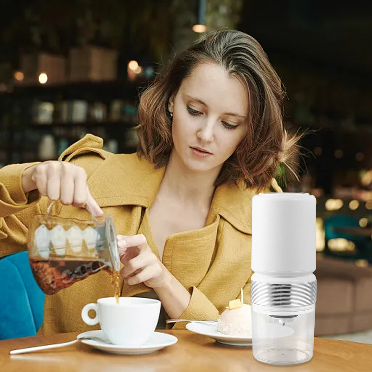 Frau gießt Kaffee aus einem Glasbehälter in eine weiße Tasse. Kleine weiße Kaffeemühle daneben.
