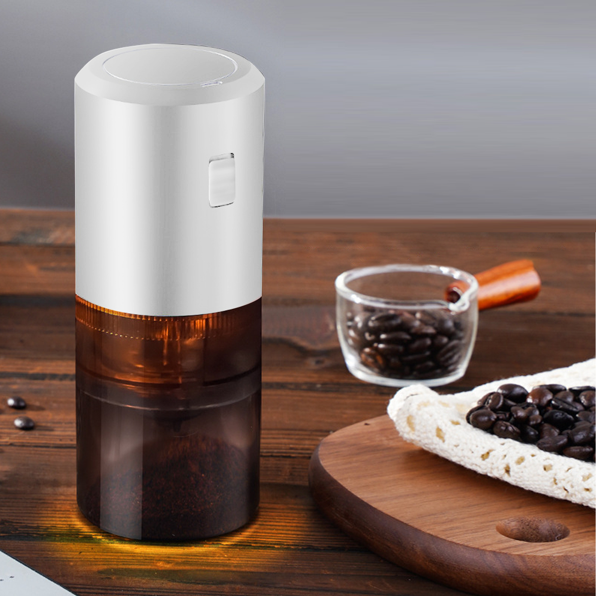 Eine elektrische Kaffeemühle mit weißem Oberteil und transparentem Behälter mit Kaffeesatz. Bohnen und Tasse liegen auf Holz.