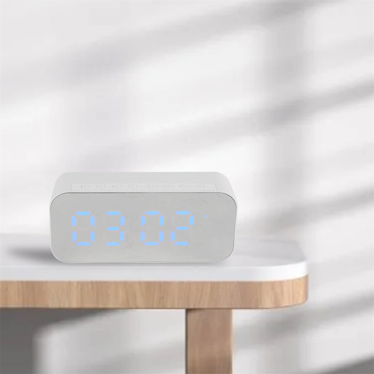 Weiße Digitaluhr mit 03:02, auf einem Holztisch.