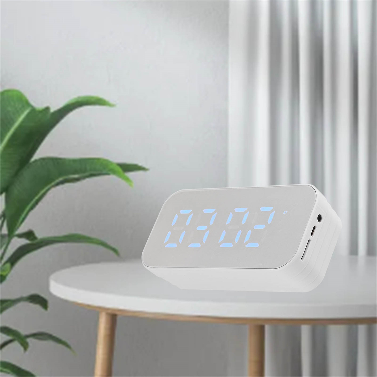 Eine weiße Digitaluhr mit blauen Zahlen auf einem weißen Tisch. Der Hintergrund ist unscharf.