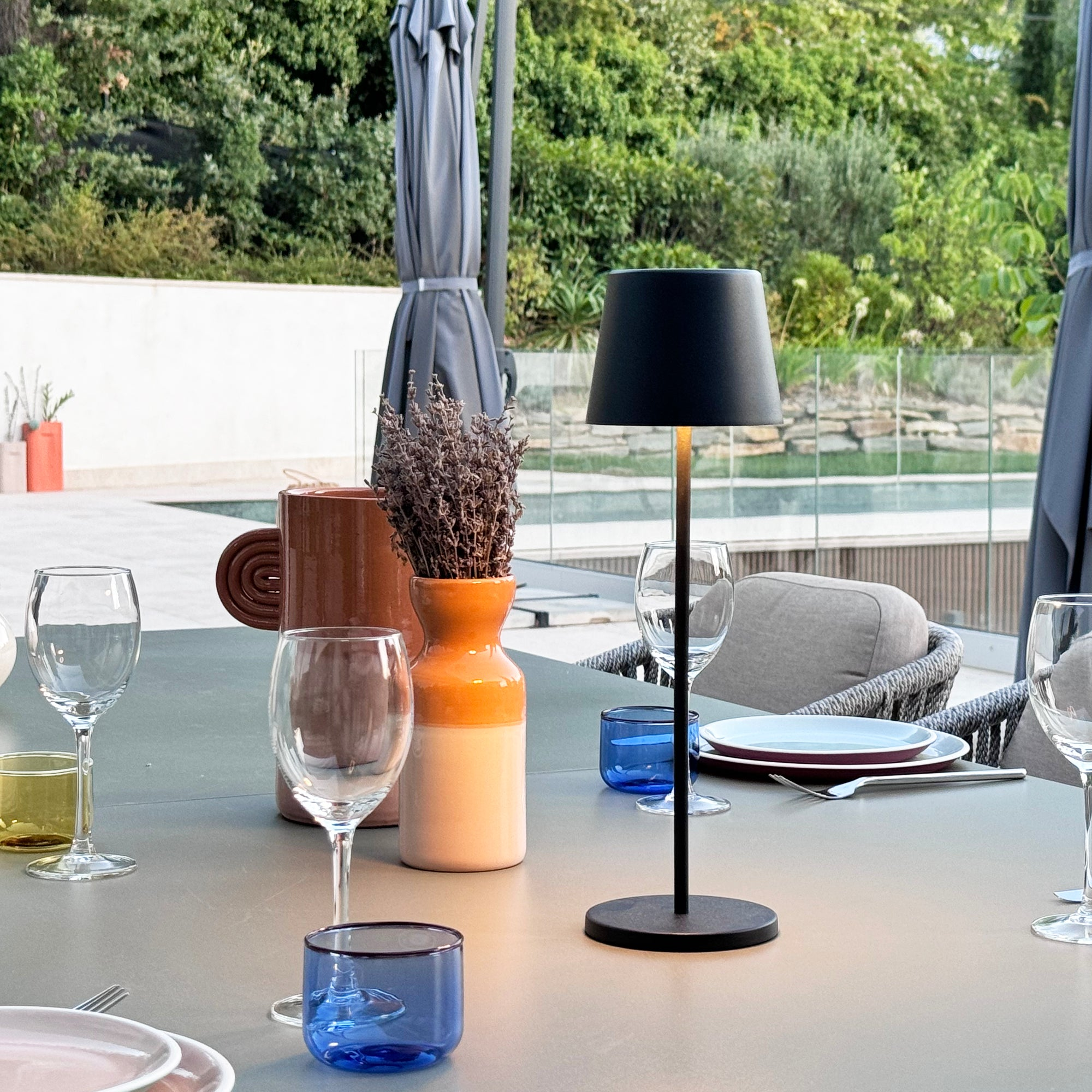 Moderne Tischdekoration im Freien mit Weingläsern und schwarzer Lampe.