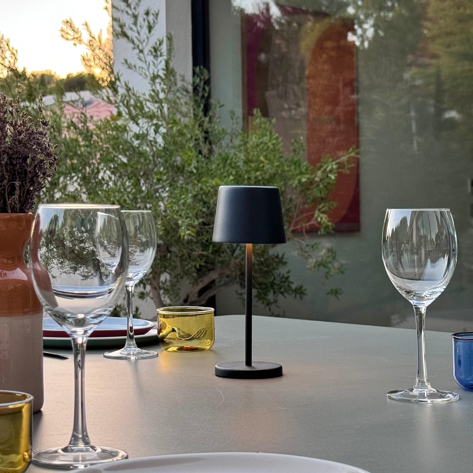 Tisch im Freien mit Weingläsern, Lampe und dekorativen Elementen.