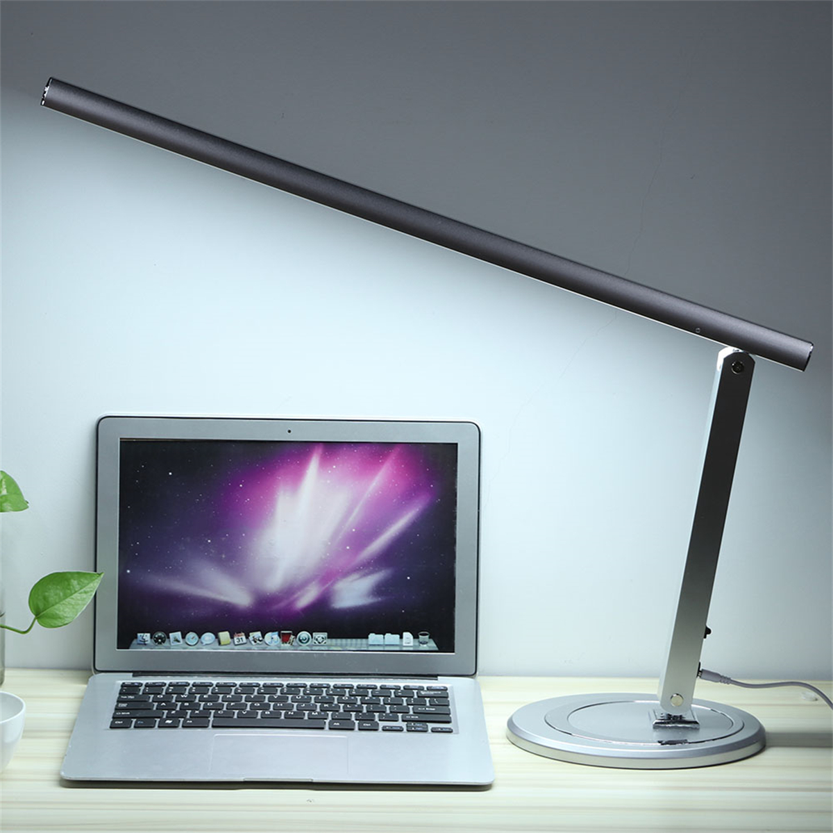 Eine moderne, silberne Schreibtischlampe mit einem langen, dünnen Lichtbalken und einem Laptop.