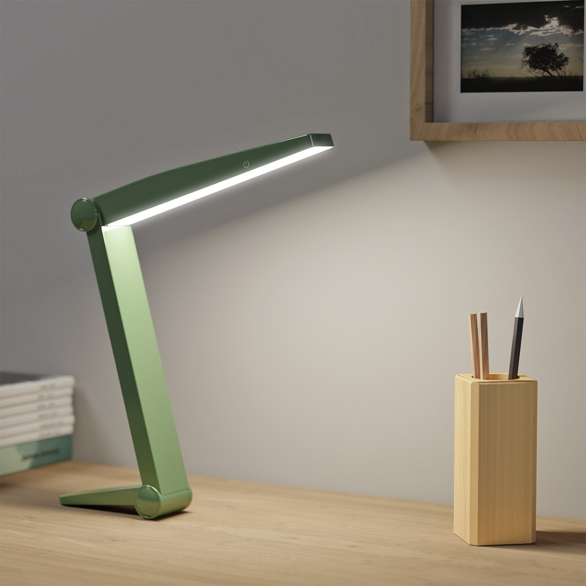 Grüne Schreibtischlampe, beleuchtet, auf einem Holzschreibtisch, neben einem Holz-Stifthalter und einem gerahmten Bild.