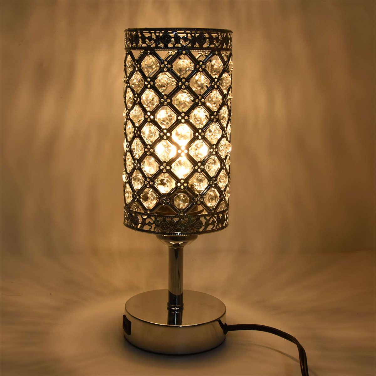 Eine kristallbedeckte Lampe mit silbernem Sockel, die Licht auf einen beigen Hintergrund wirft.