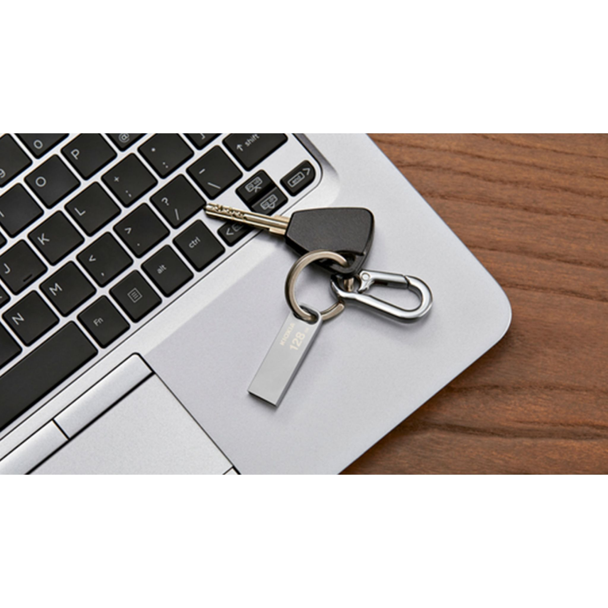 Srebrny pendrive i klucz na klawiaturze laptopa, obok drewnianej powierzchni.