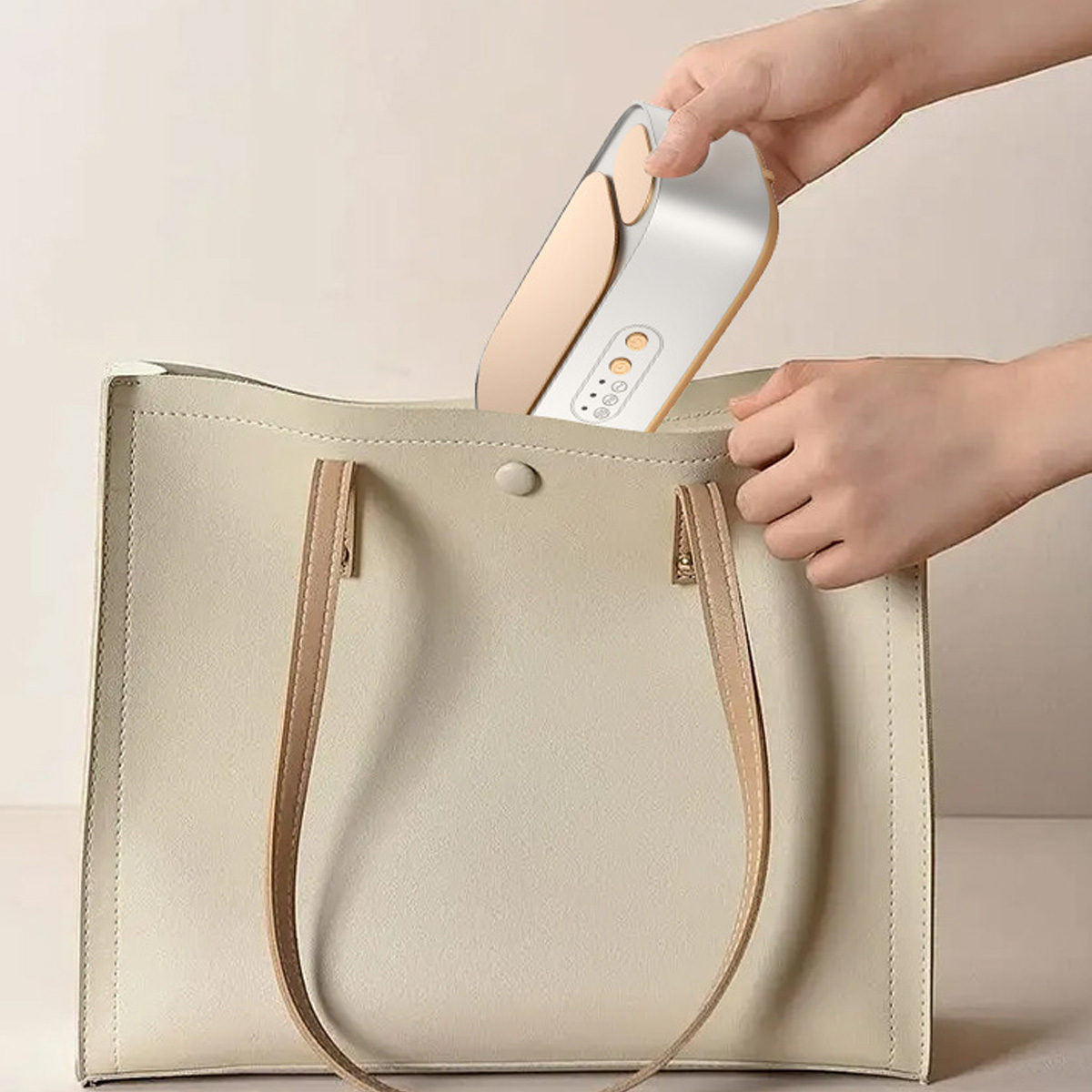 Person legt ein kleines elektronisches Gerät in eine cremefarbene Handtasche.