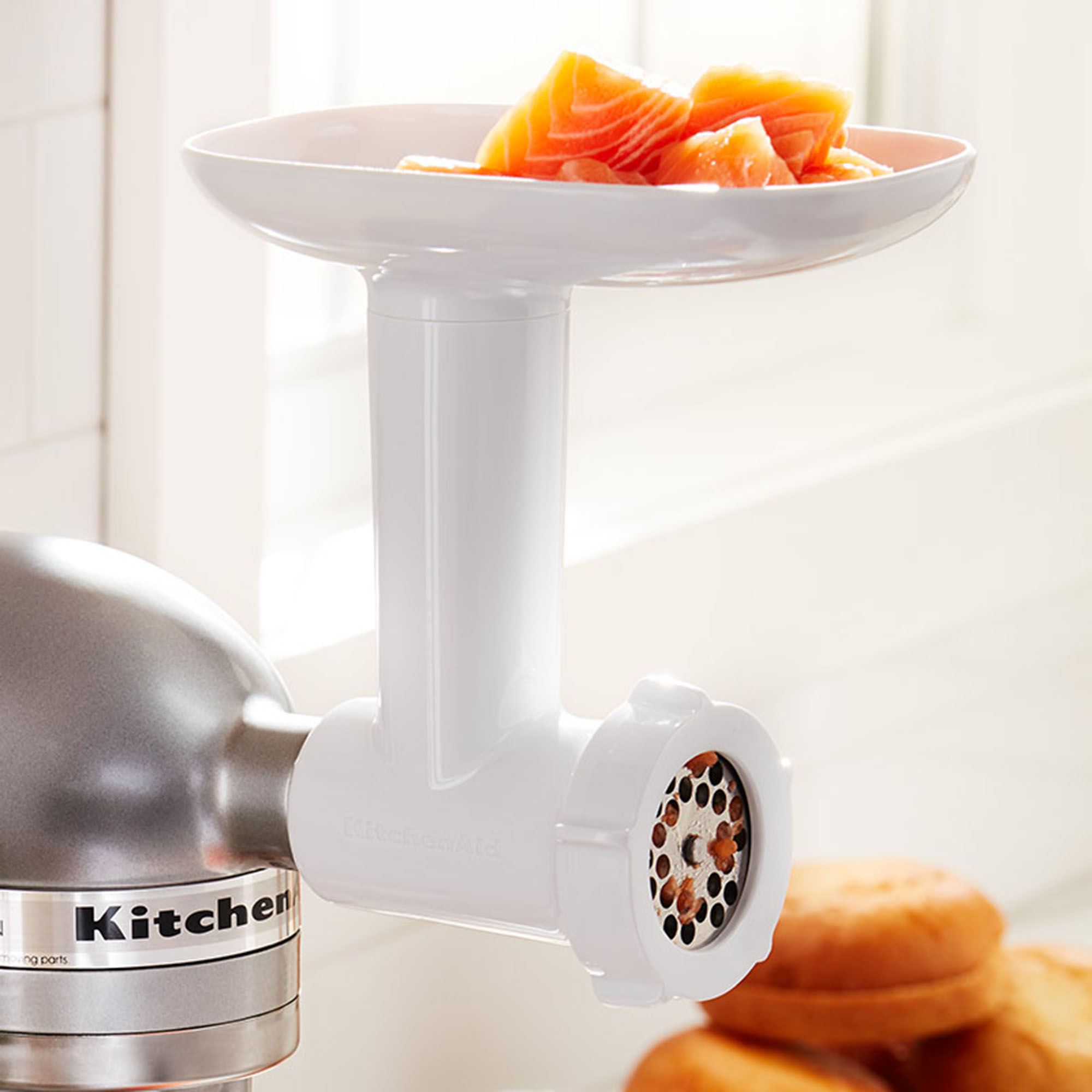 Białe akcesorium do mielenia mięsa KitchenAid z kawałkami łososia w górnej tacy.