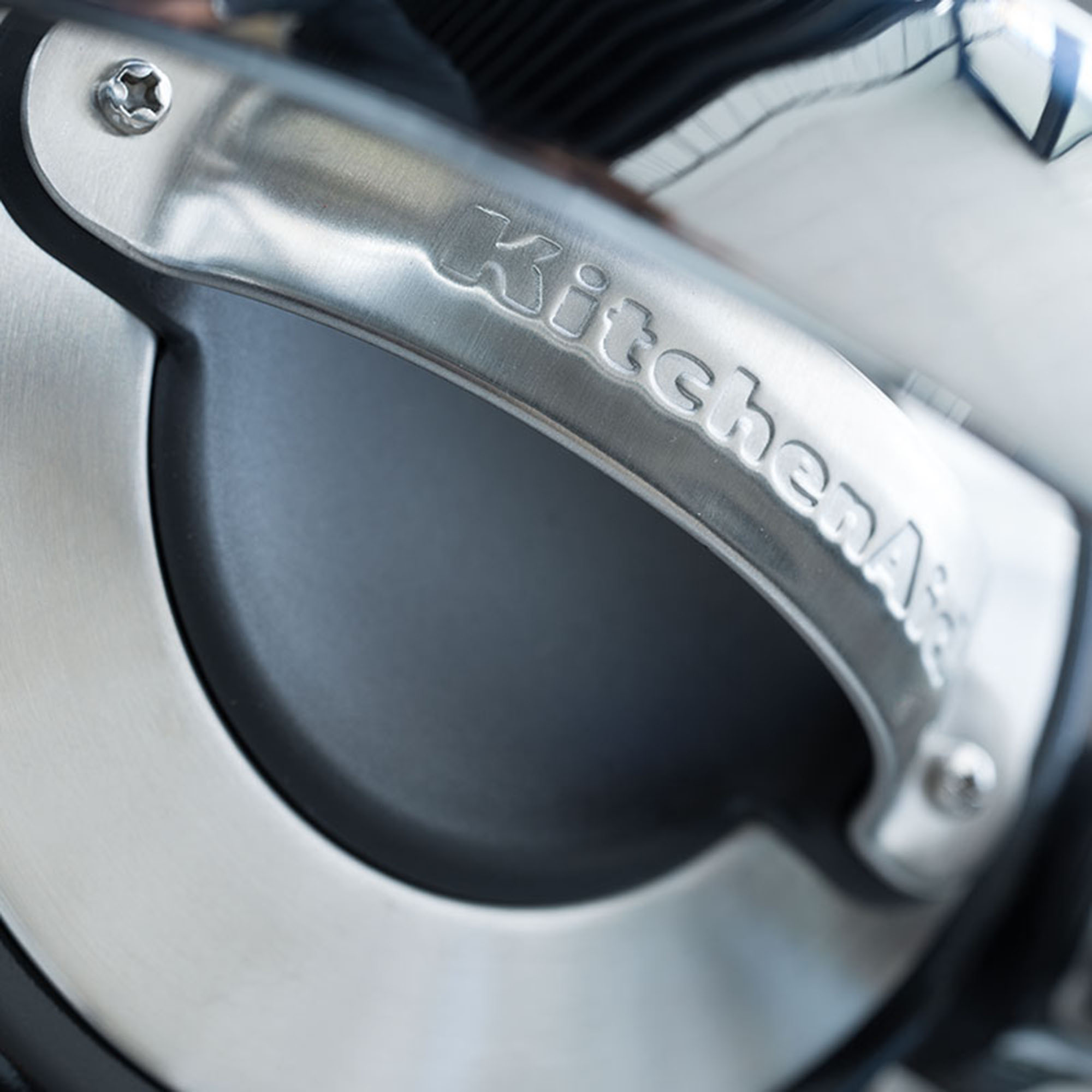 Close-up of a KitchenAid mixer handle, made of silver metal. The word "KitchenAid" is embossed.