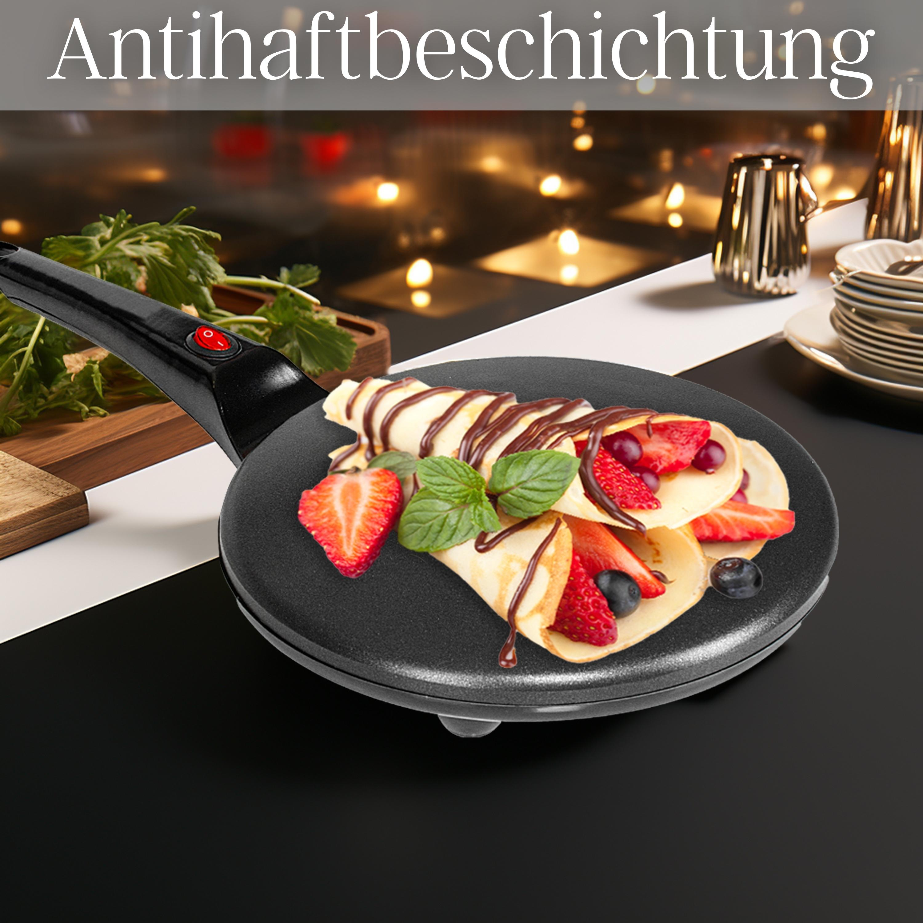 Crêpe auf schwarzer Pfanne mit Erdbeeren, Blaubeeren und Schokosirup, Minze, auf einem Tisch.