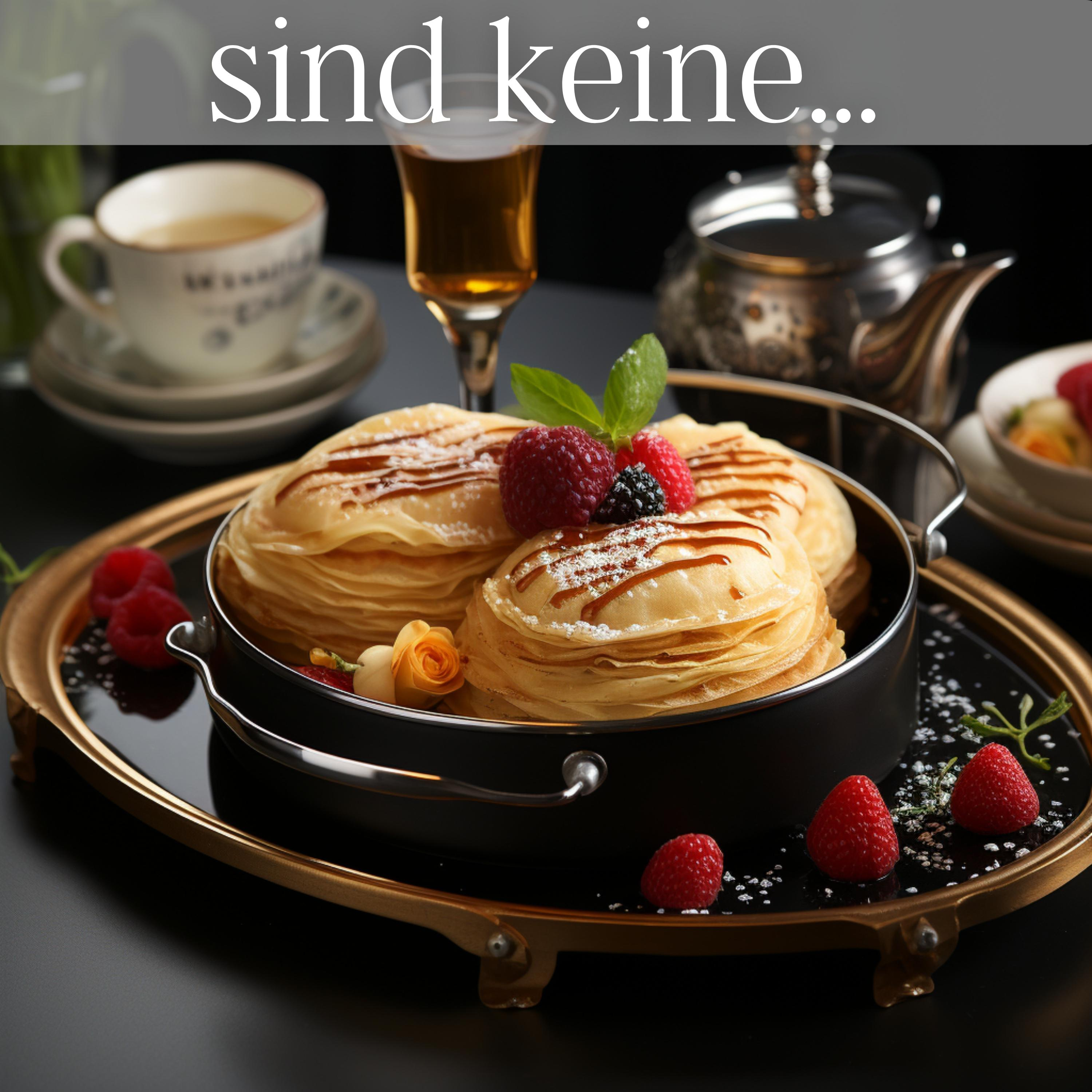 Pfannkuchen mit Himbeeren und Karamell auf einem schwarzen Teller. Eine Tasse Tee, ein Glas und eine Teekanne im Hintergrund.