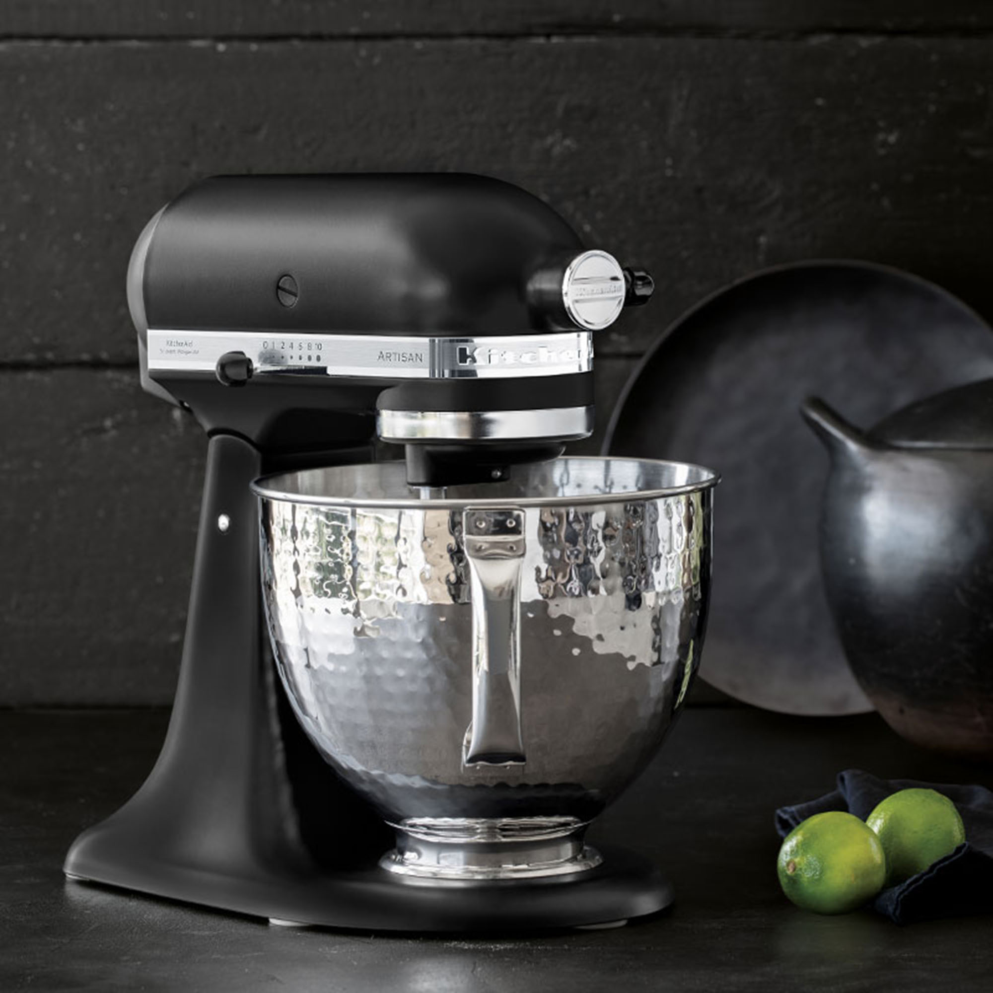 Schwarzer KitchenAid-Küchenmixer mit Edelstahlschüssel, Limetten und dunklem Hintergrund.