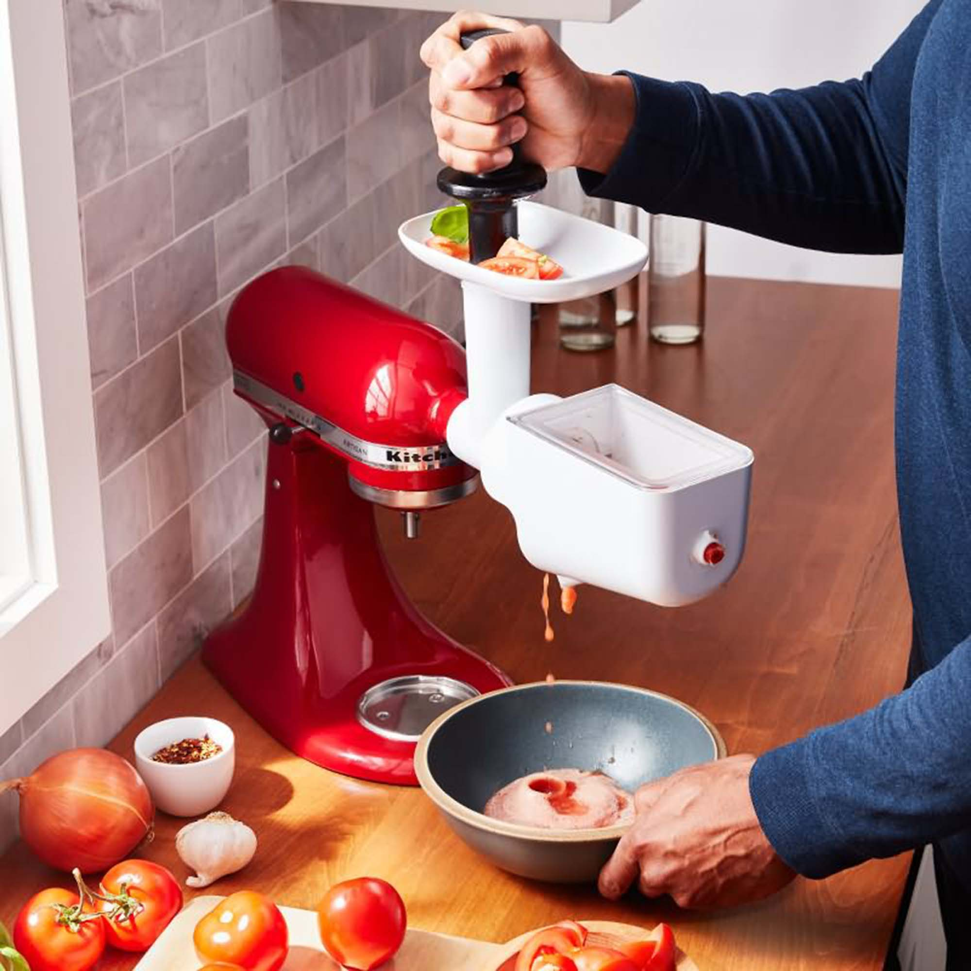 Frullatore KitchenAid rosso con accessorio per robot da cucina, usato da una persona.