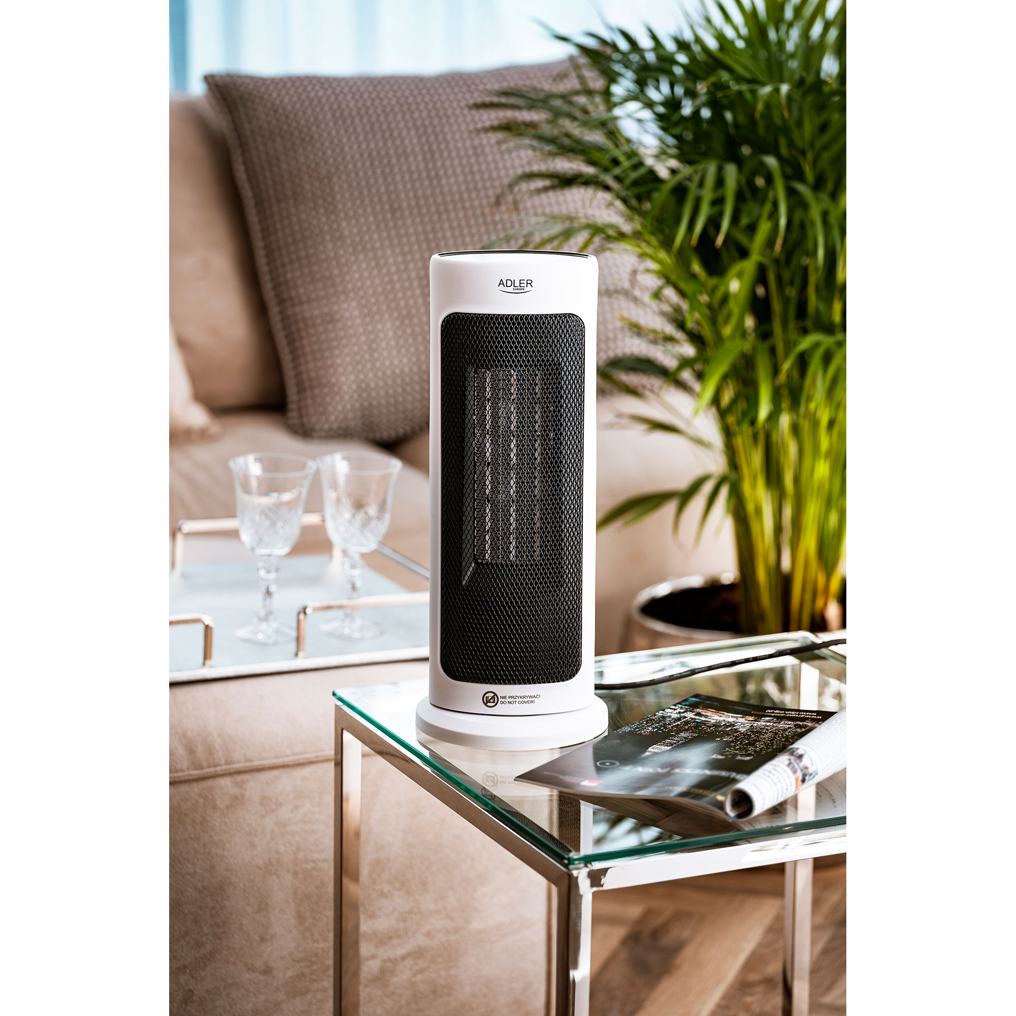 Calentador de torre blanco y negro en mesa de cristal, en habitación con sofá y planta.