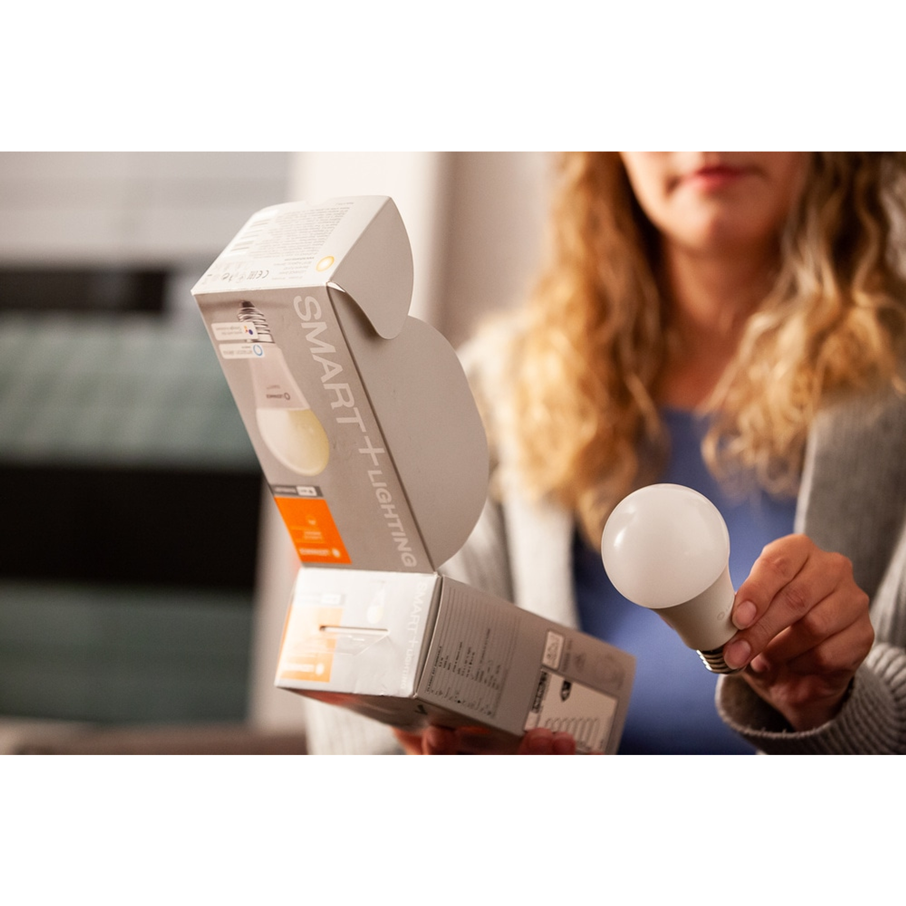 Osoba trzymająca inteligentne żarówki i pudełko; rozmyte tło.