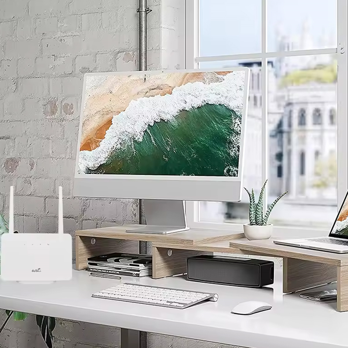 Schreibtisch mit Computer, Monitor, Lautsprecher, Router und Fenster mit Stadtblick.