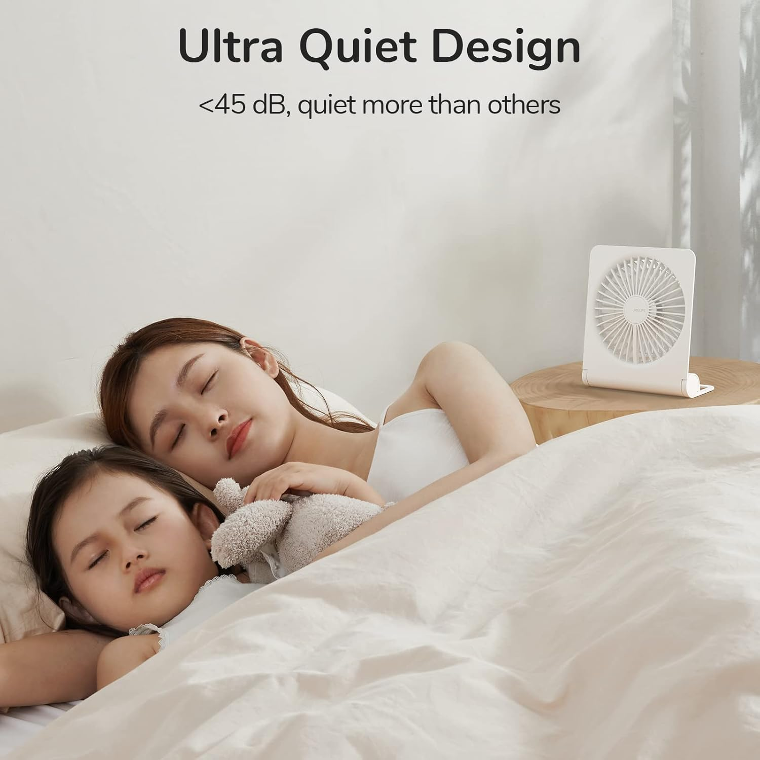 Zwei Frauen schlafen im Bett. Ein weißer Ventilator steht auf einem Holztisch.