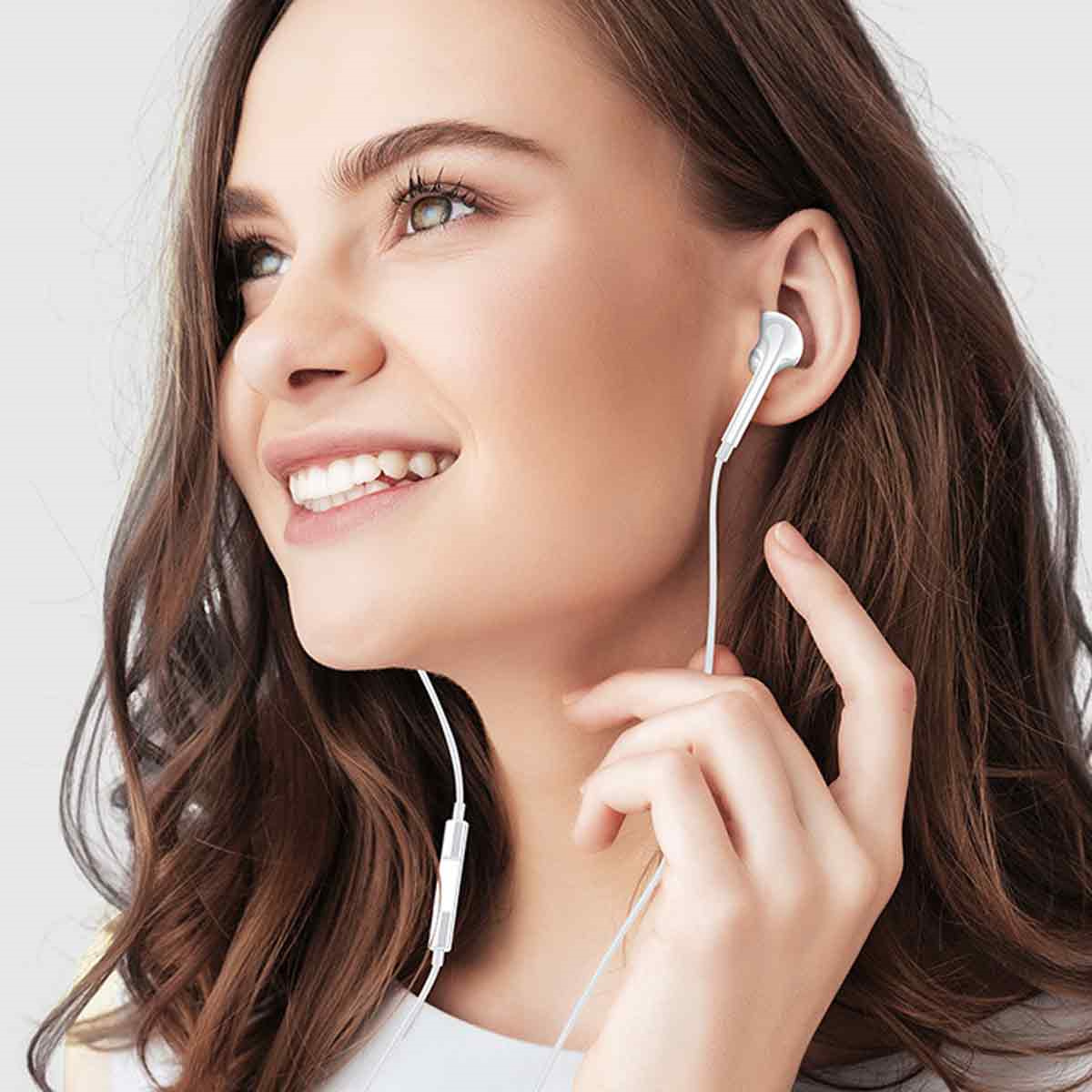 Eine Frau mit weißen Ohrhörern, die lächelt, wobei die Ohrhörer durch ein weißes Kabel verbunden sind.