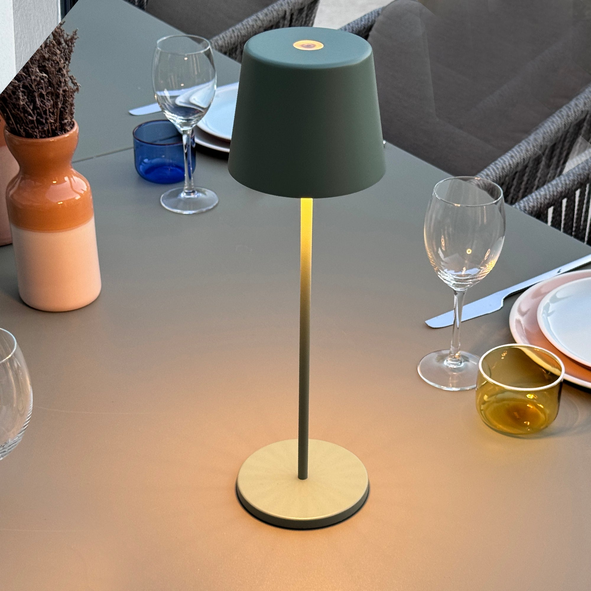 Tisch im Freien mit Lampe, Weingläsern und dekorativen Vasen.