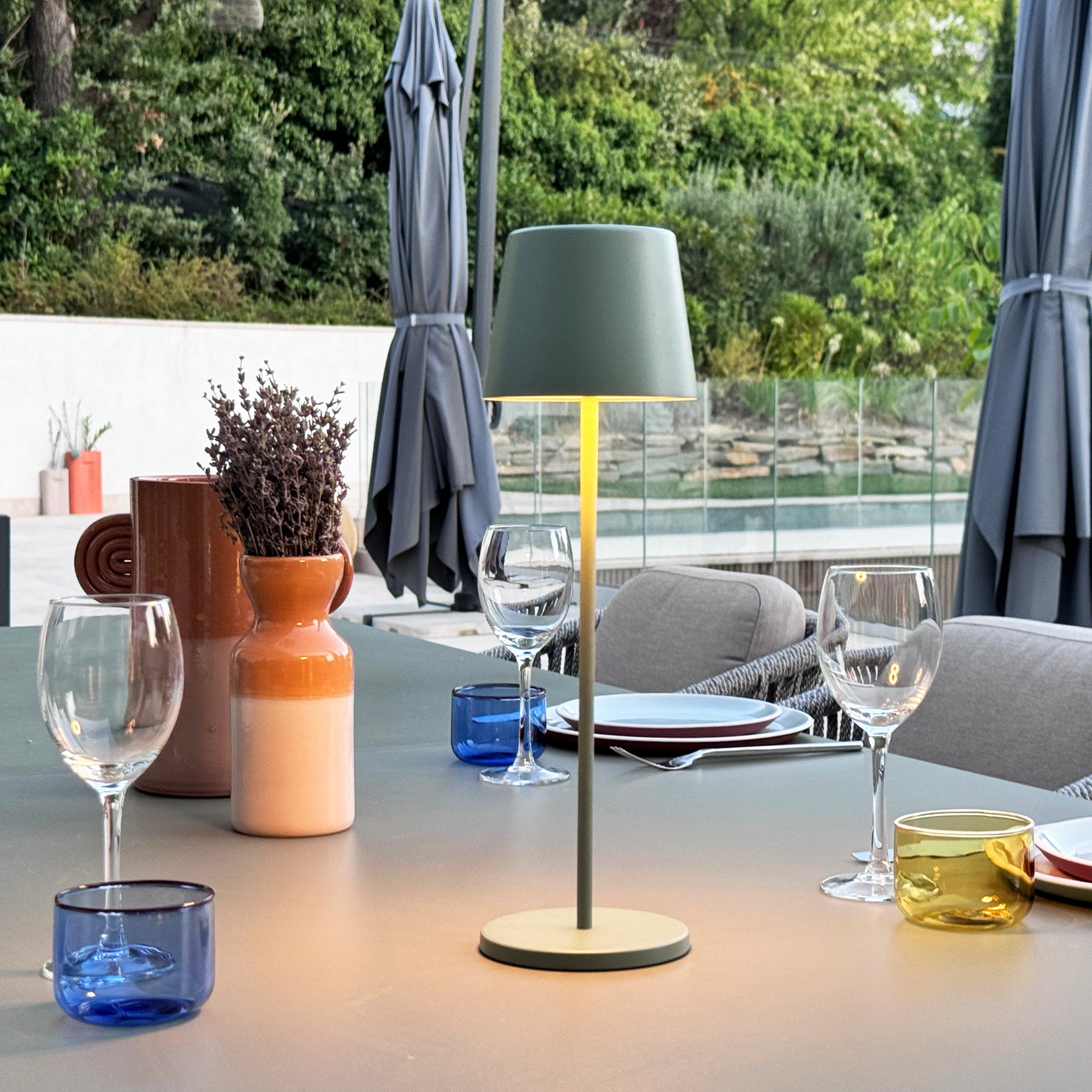 Szene im Freien mit Tisch, Lampe, Gläsern und Sonnenschirmen. Grüner Hintergrund.