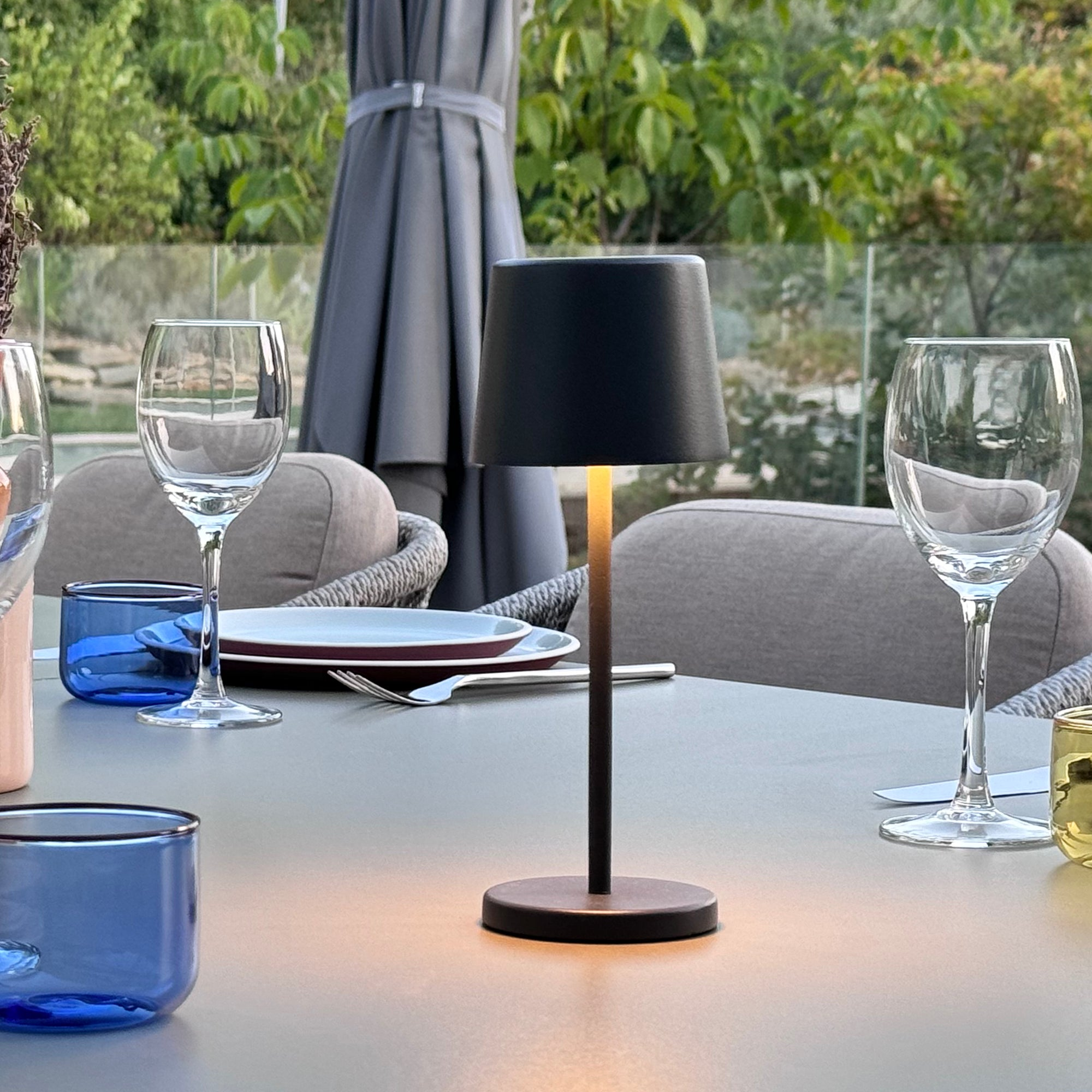 Tischarrangement mit kleiner Lampe, Weingläsern, blauen Gläsern, Tellern und verschwommenem Hintergrund.