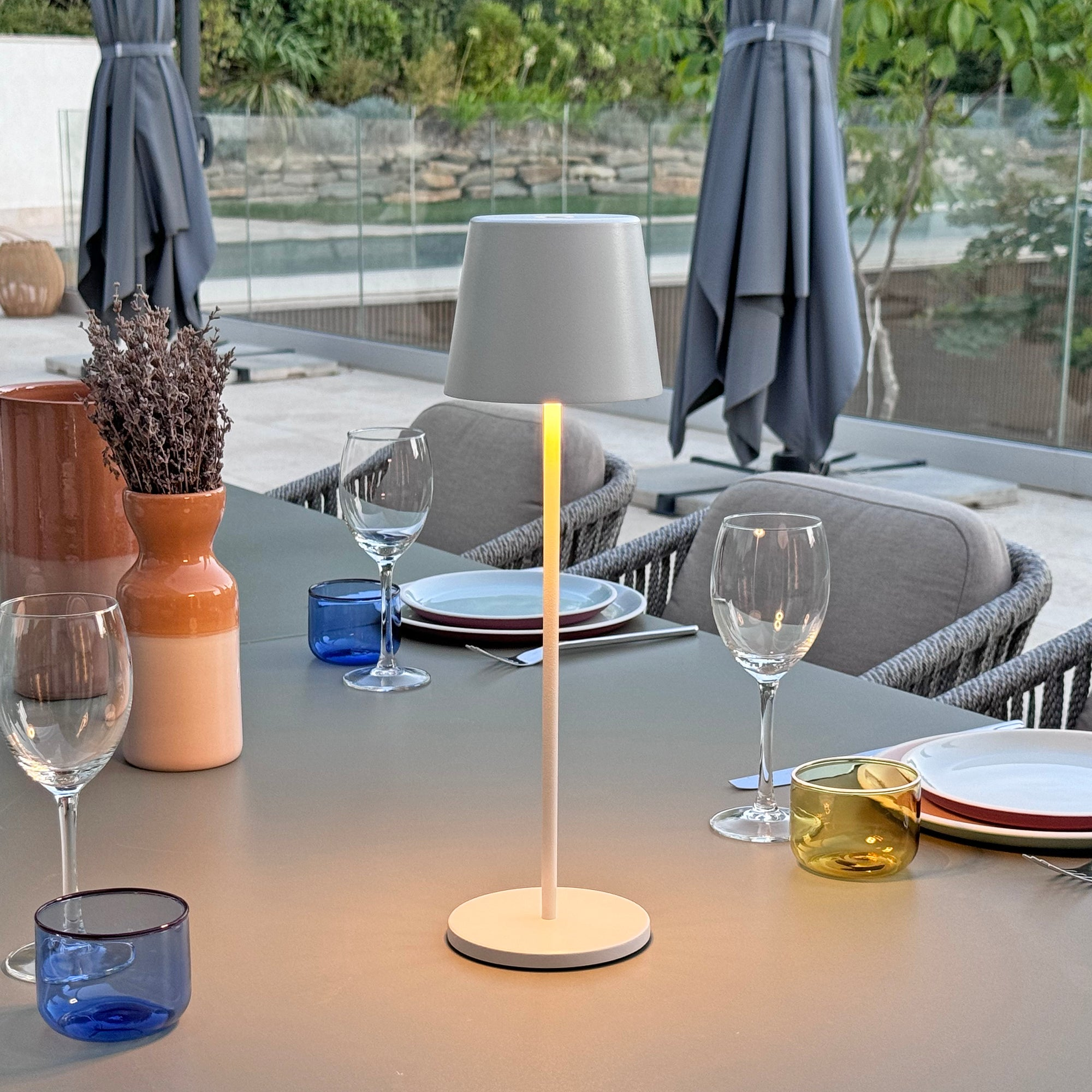 Tischlampe, Gläser und Deko auf dem Tisch. Outdoor-Terrassenszene. Sonnenschirme.