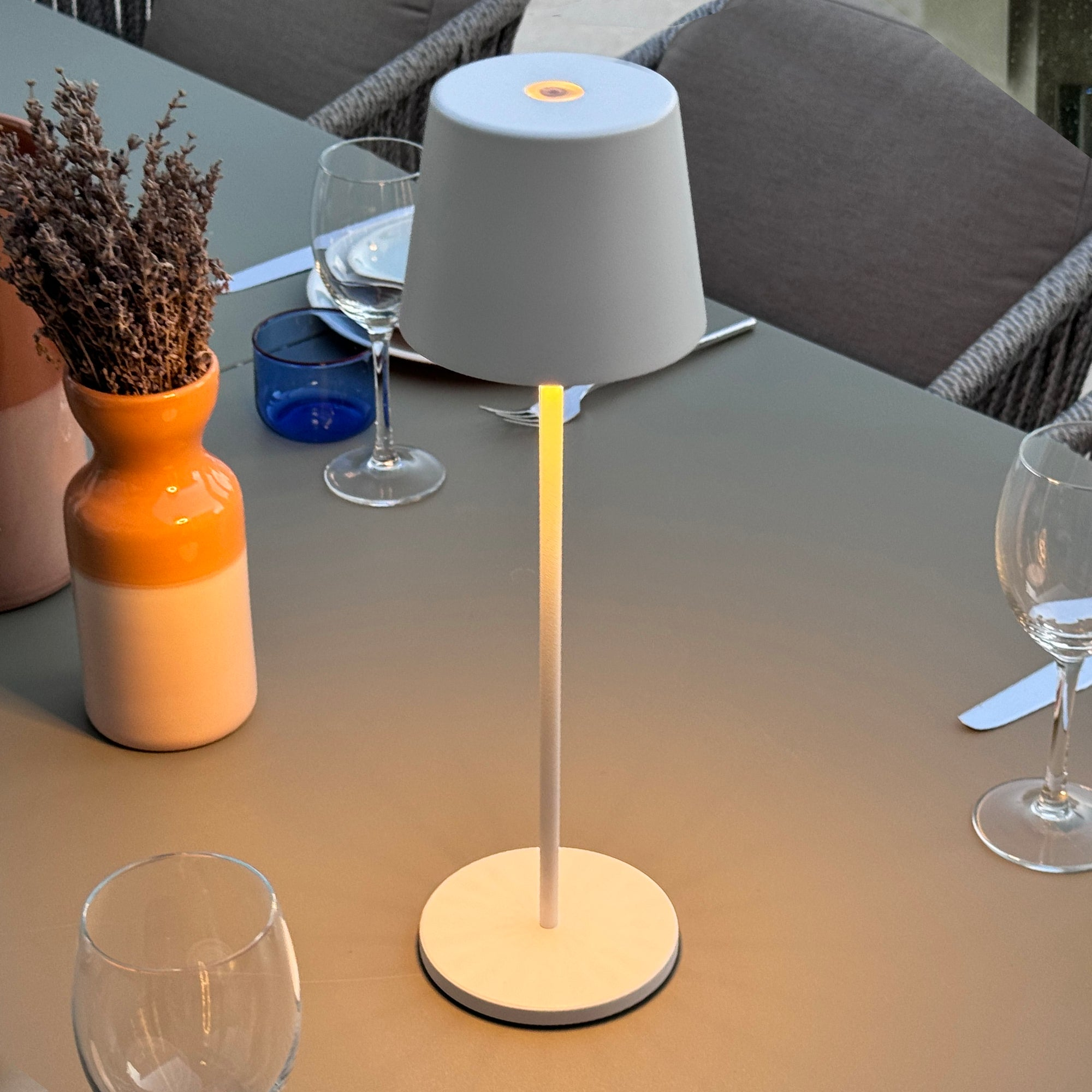 Tisch im Freien mit Lampe, Gläsern, Vase und einer Flasche.