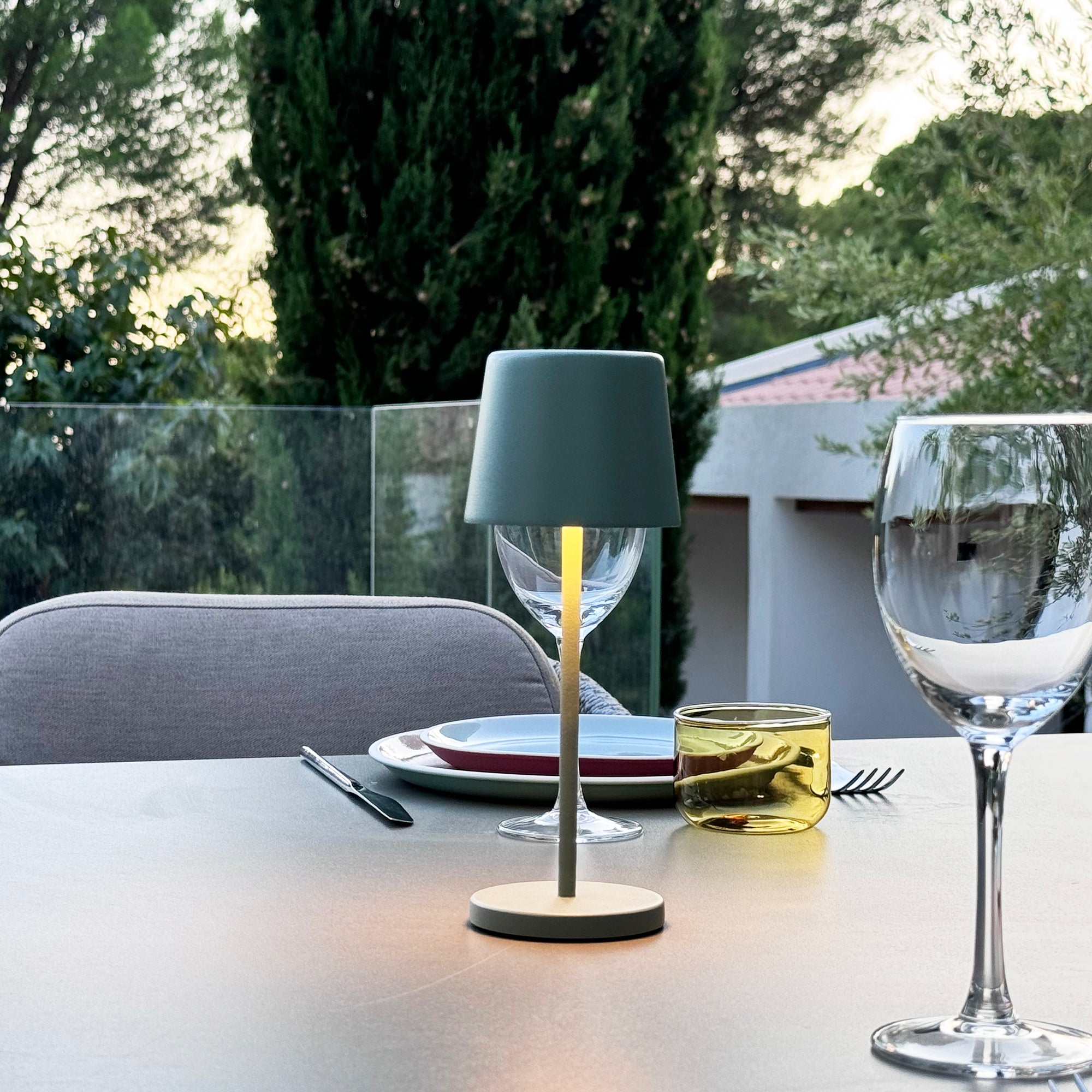 Moderne Outdoor-Tischdekoration mit Lampe, Gläsern und Teller.