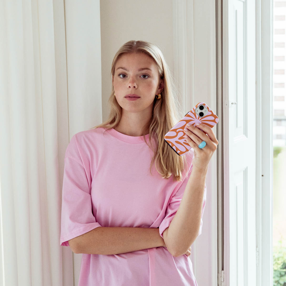 Vrouw die een telefoon met hoes vasthoudt. Ze staat bij een raam.