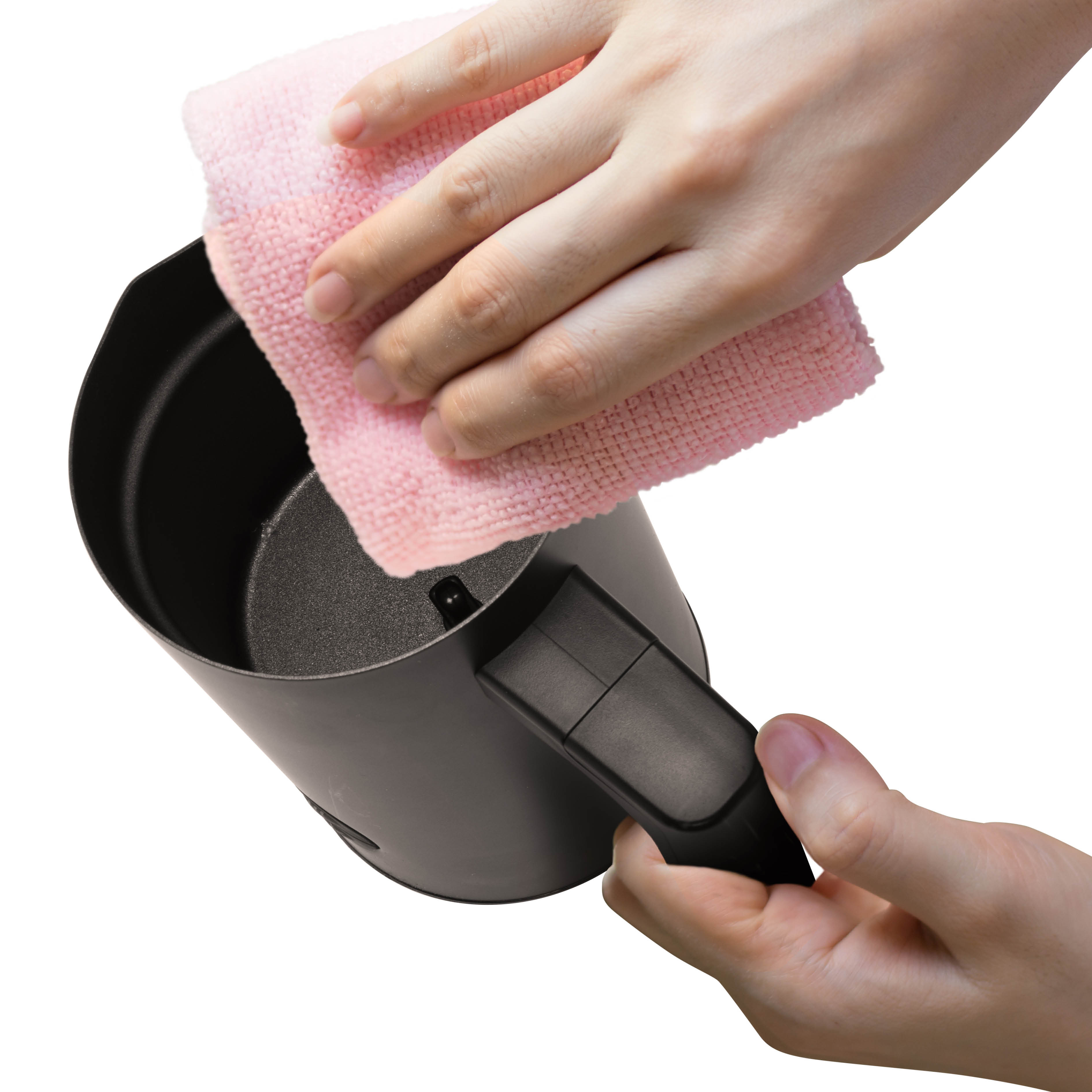 Des mains nettoient une casserole noire avec un chiffon rose.