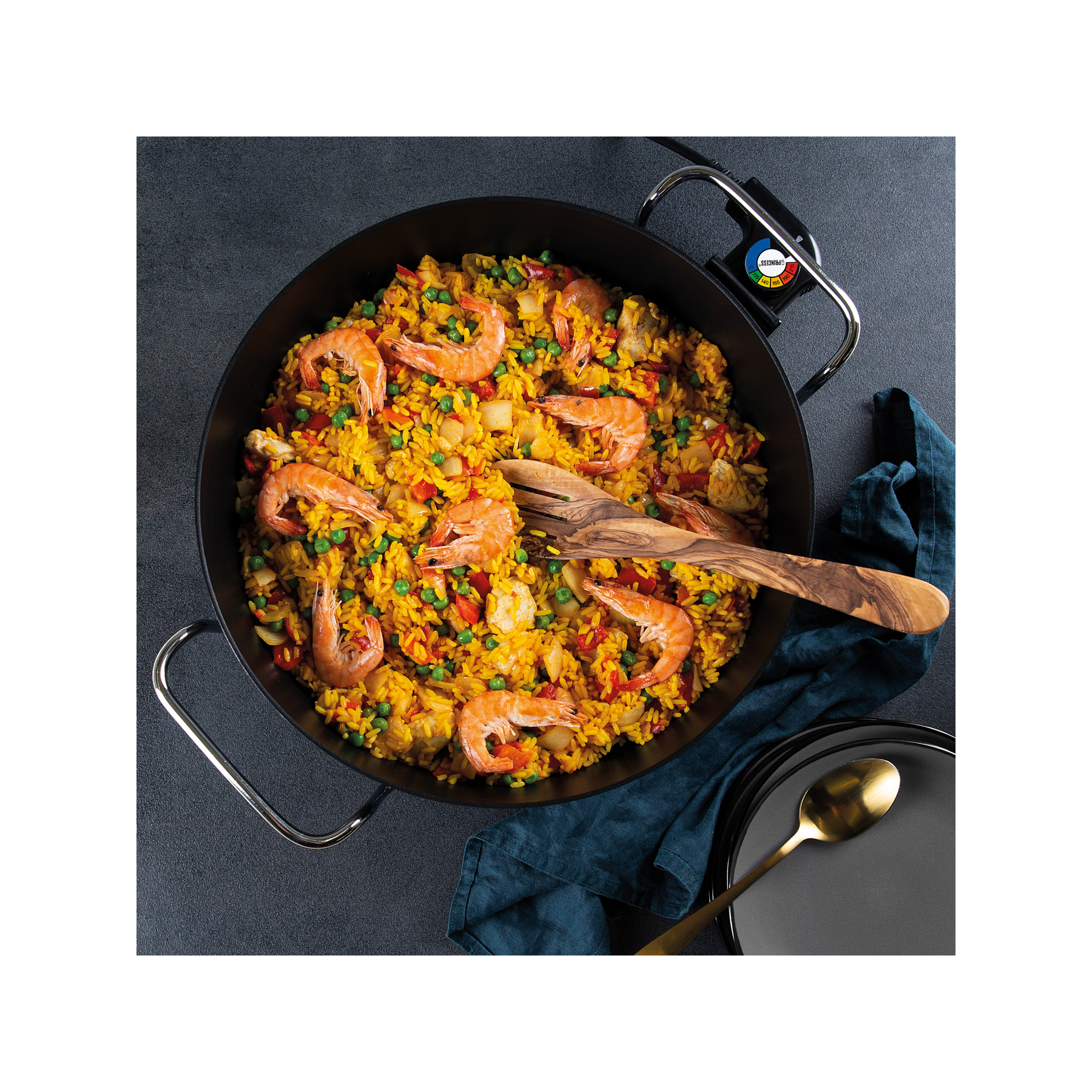 Een pan paella met garnalen en groenten, met een houten lepel.