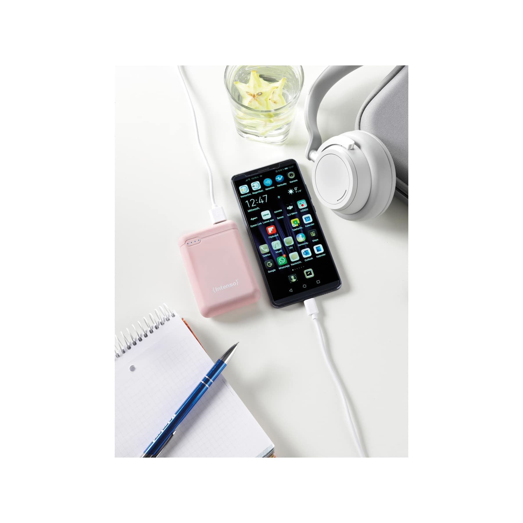 Telefon, das mit einer Powerbank geladen wird. Daneben sind Notizblock, Stift und Kopfhörer zu sehen.