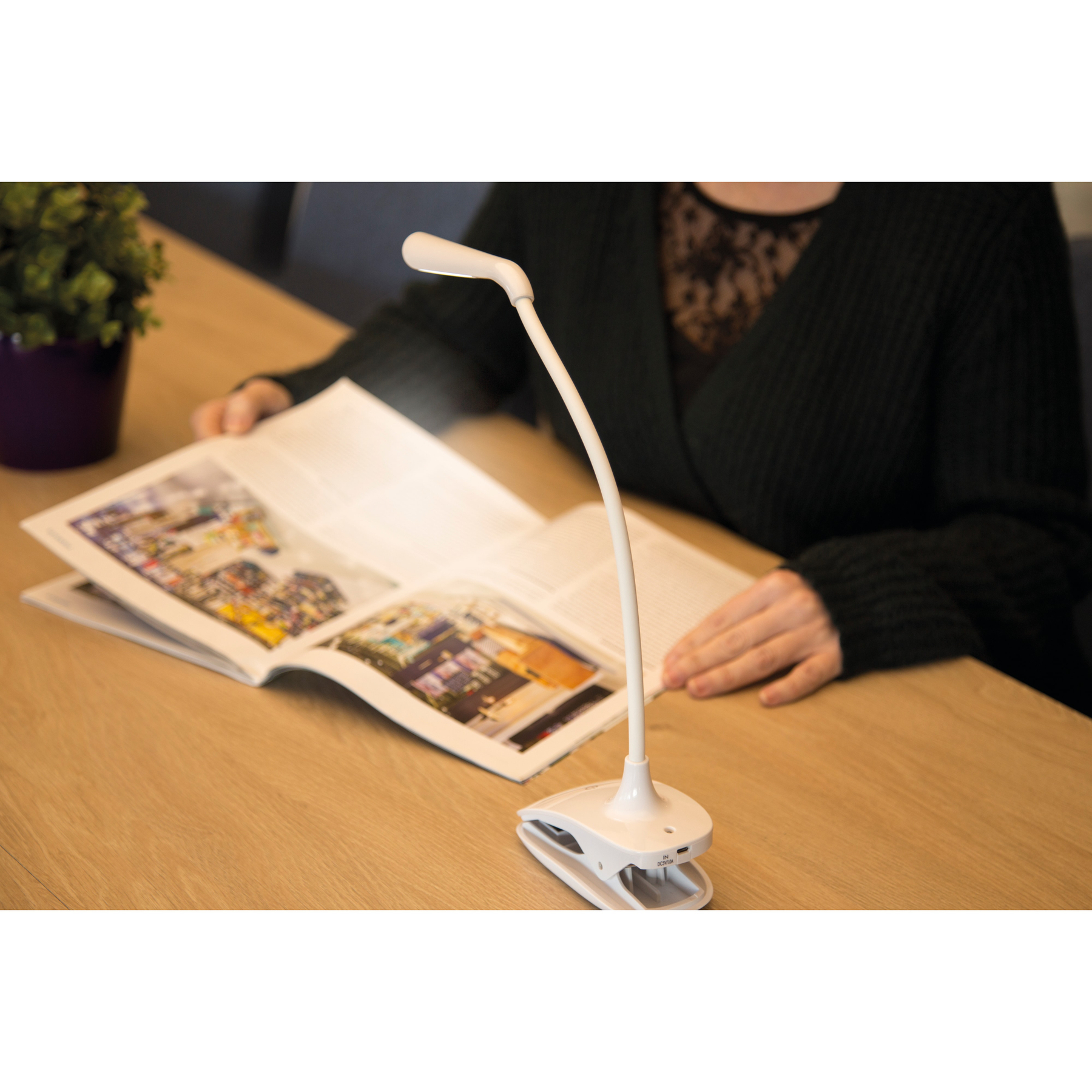 Een bureaulamp op een tafel met een boek en een persoon die leest.