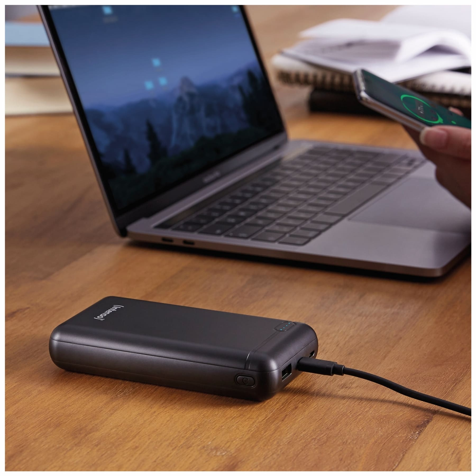 Ein Laptop, eine Powerbank mit Kabel und eine Person, die ein Telefon hält.