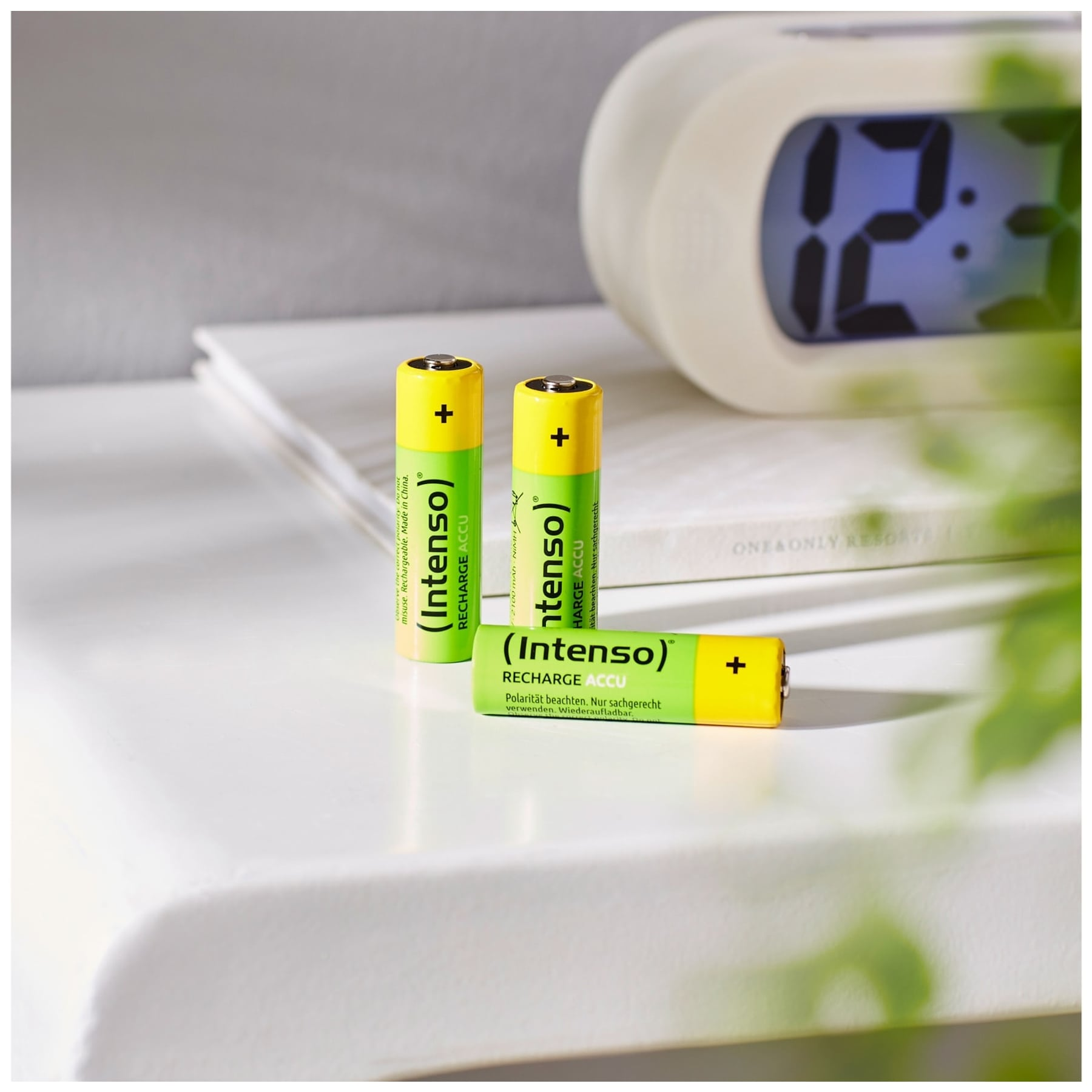 Trzy akumulatory z logo Intenso na białej powierzchni obok zegara.
