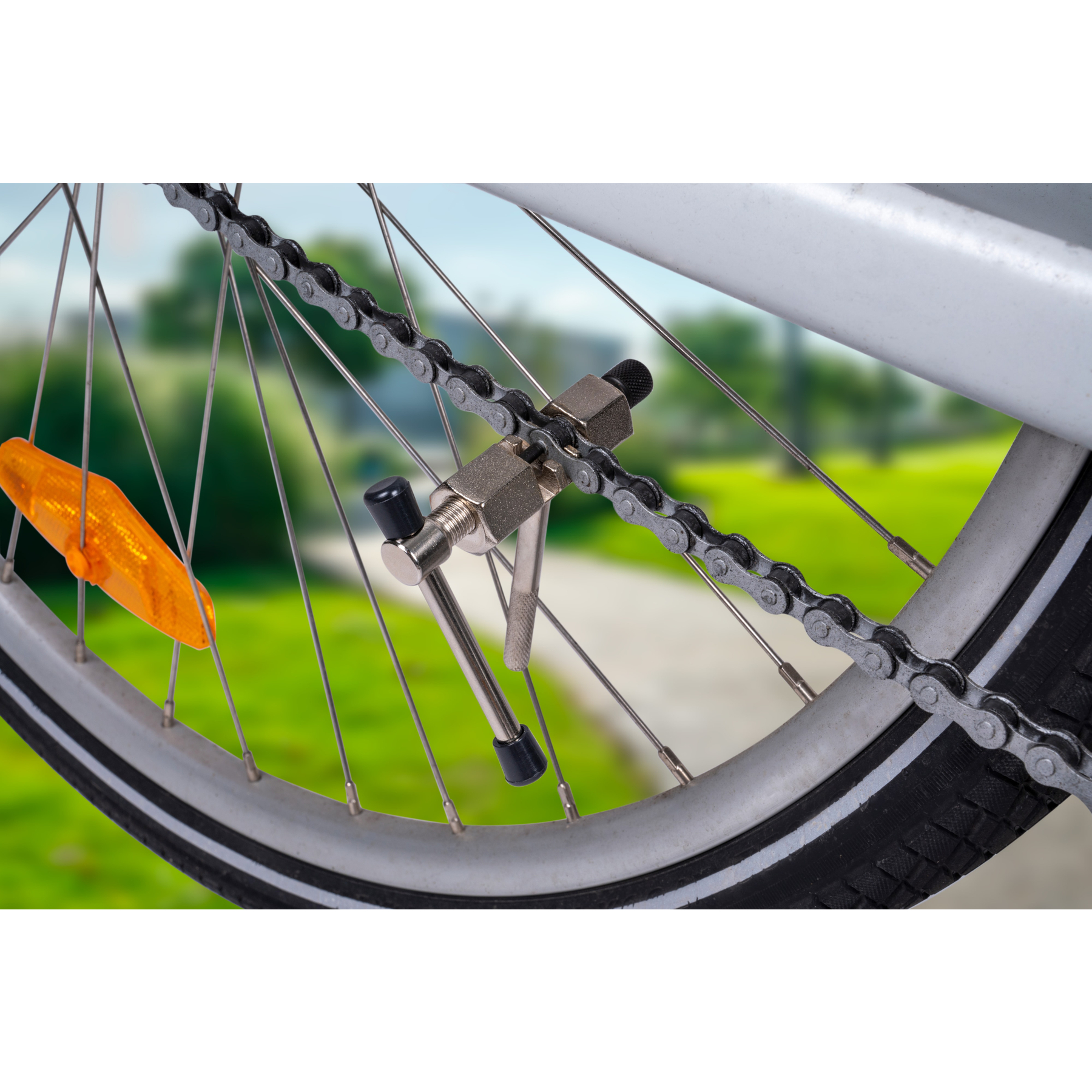 Eine Fahrradkette wird mit einem Kettenwerkzeug repariert. Der Hintergrund zeigt einen grünen Park.