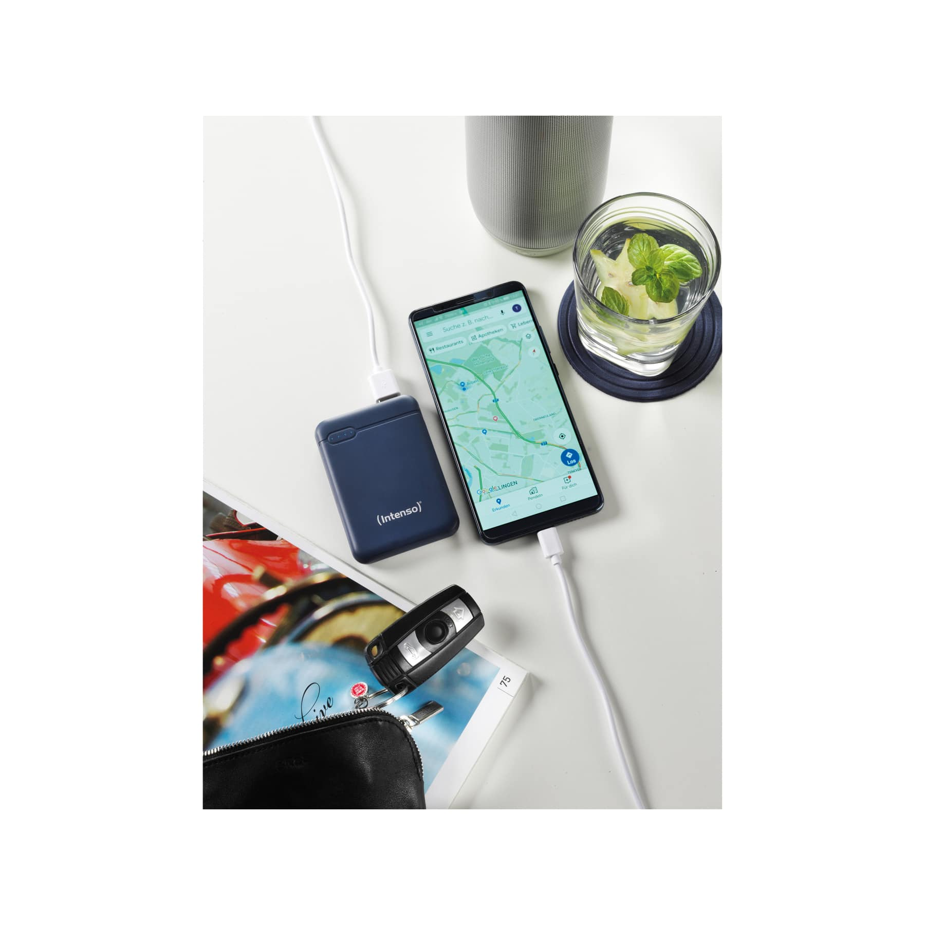 Telefono e power bank collegati da un cavo, accanto a un bicchiere d'acqua.