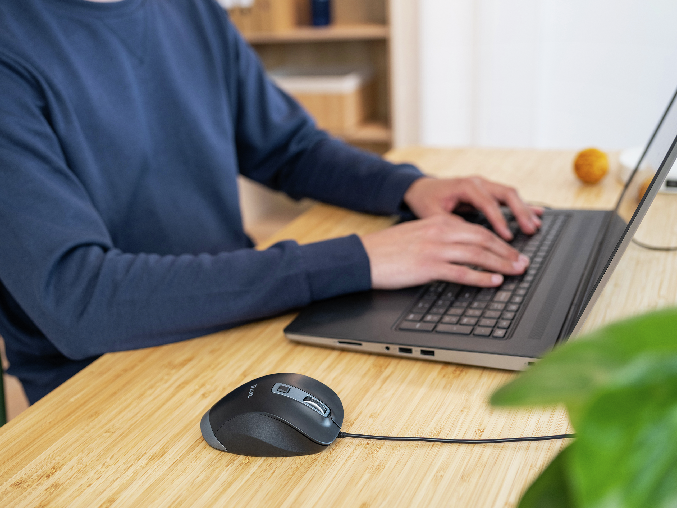 Eine Person tippt auf einem Laptop mit einer schwarzen Maus vor sich auf einem Holztisch.