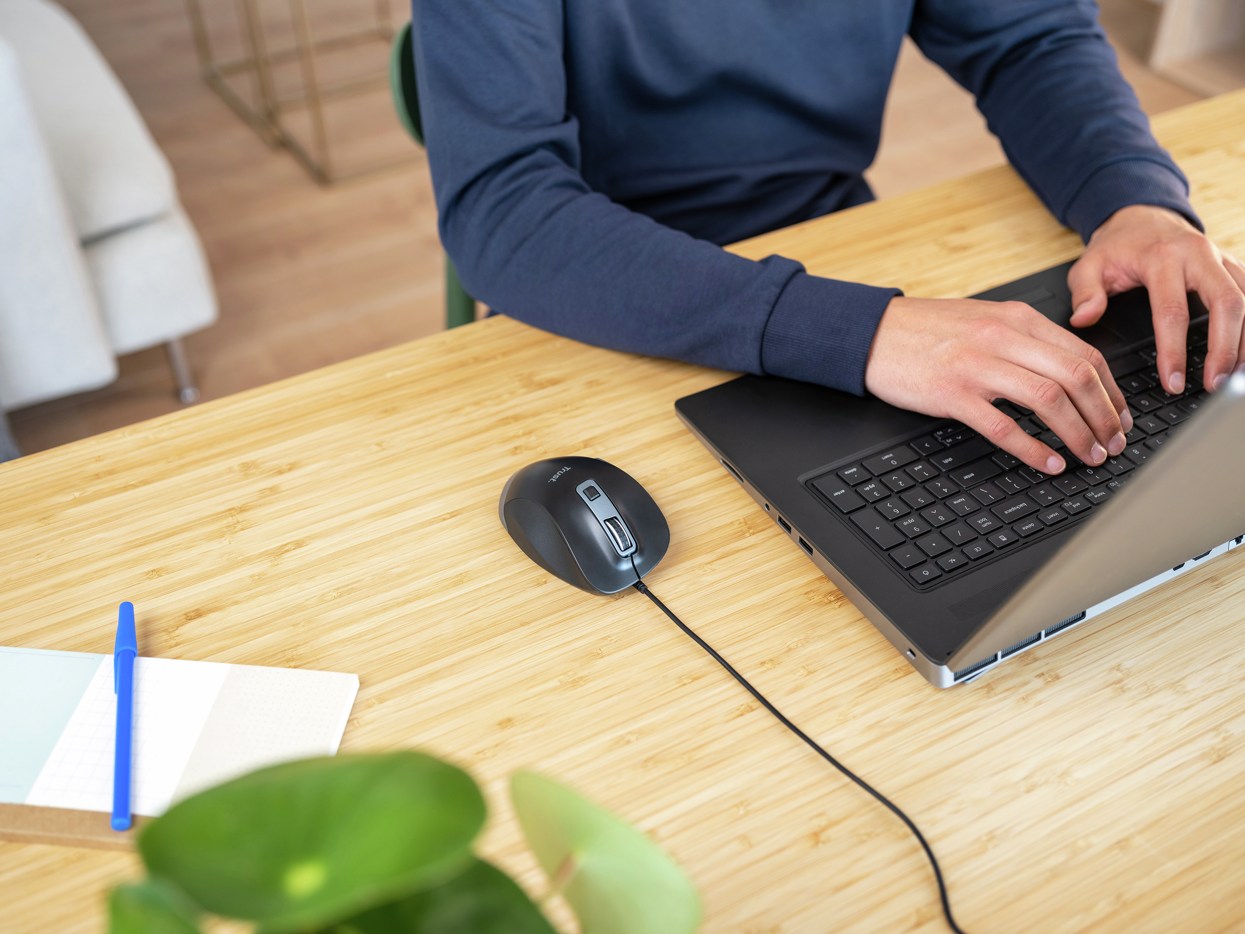 Hände einer Person, die auf einem schwarzen Laptop tippen, neben einer Maus und einem Stift.