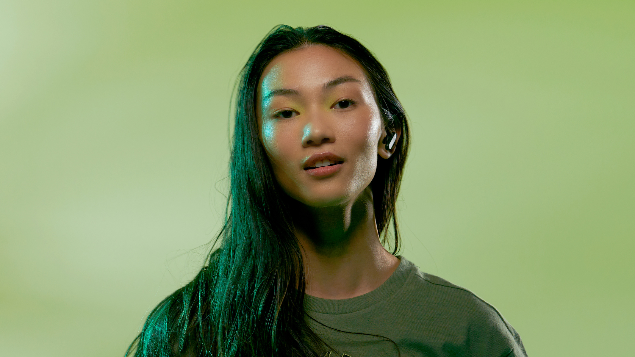 Kobieta z długimi, ciemnymi włosami patrzy w kamerę, nosząc słuchawki. Zielone tło.